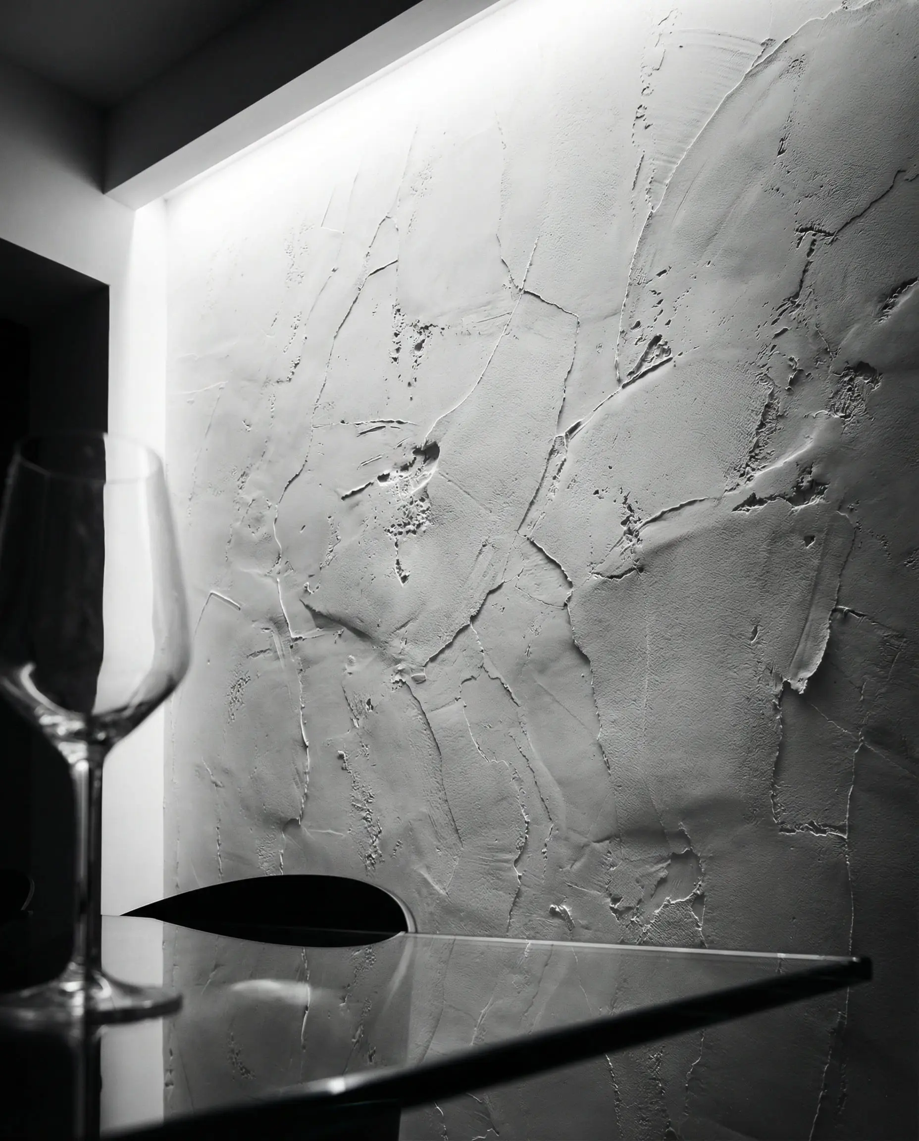 Architectural detail showing LED grazing light illuminating the ridges and imperfections of a white hand-troweled microcement wall.