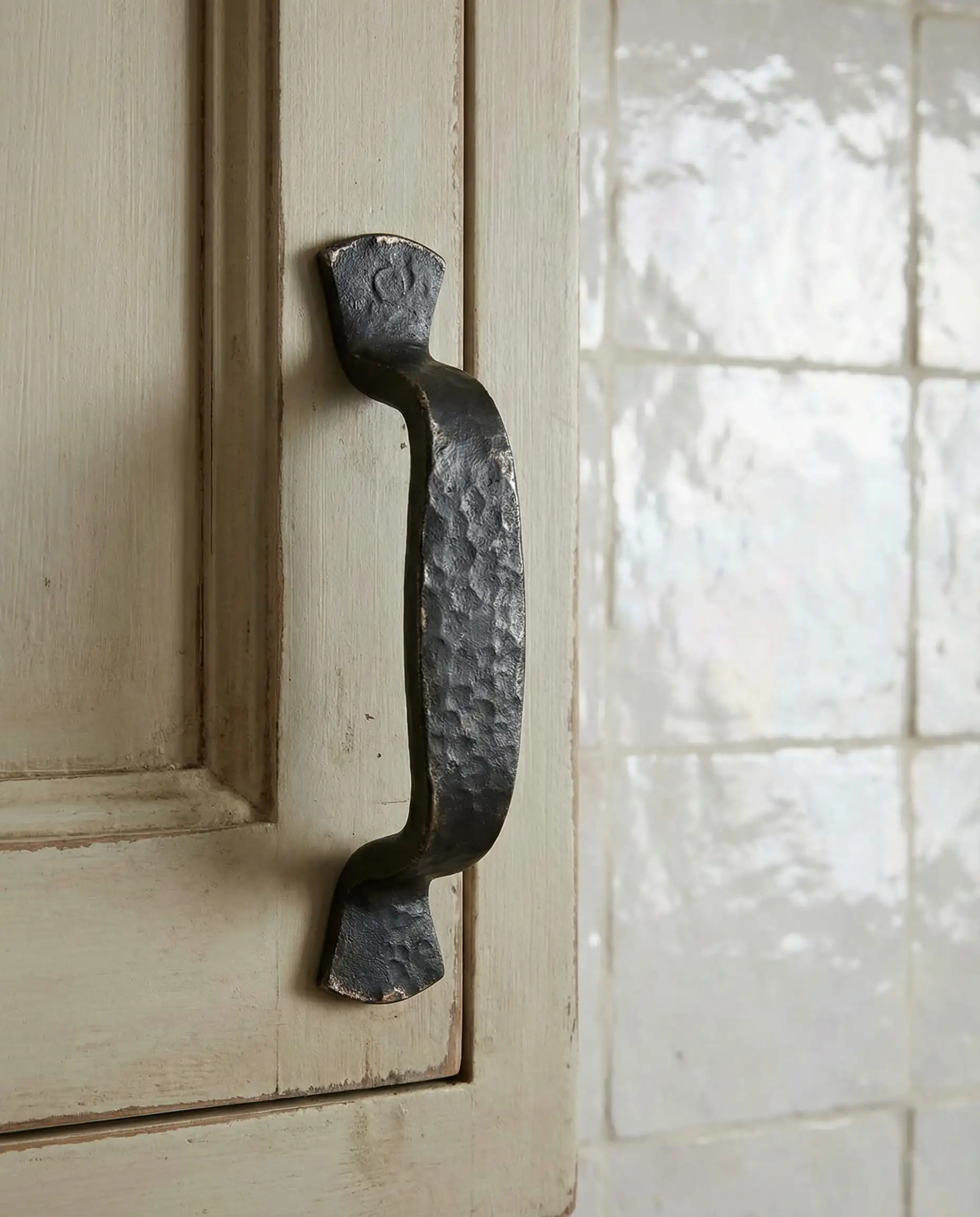 Close-up of hand-forged iron black hardware with hammered texture set against pearlescent white Zellige tiles.