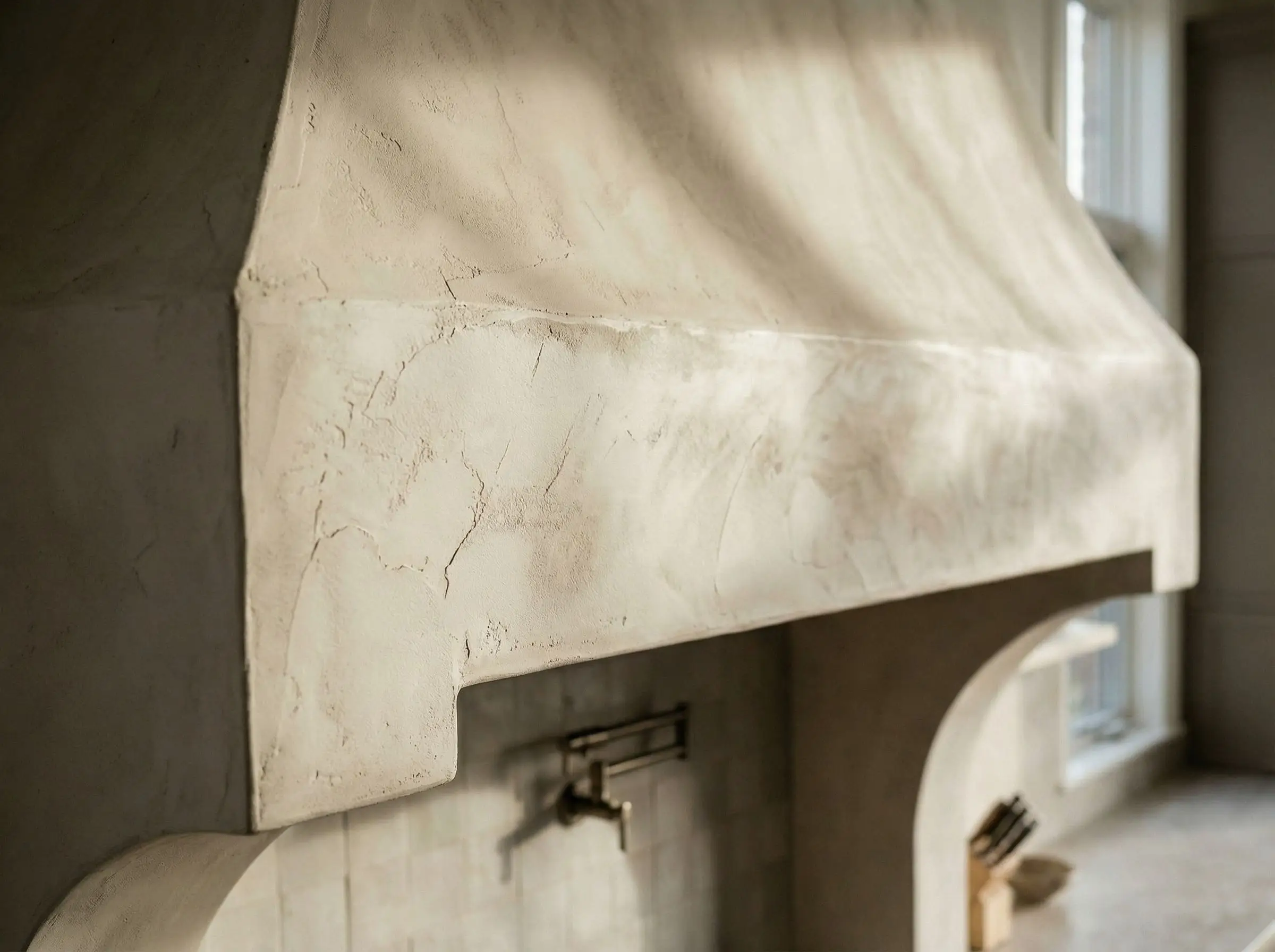 A close view reveals the chalky texture and rolling shadows of a hand-troweled plaster range hood surface.