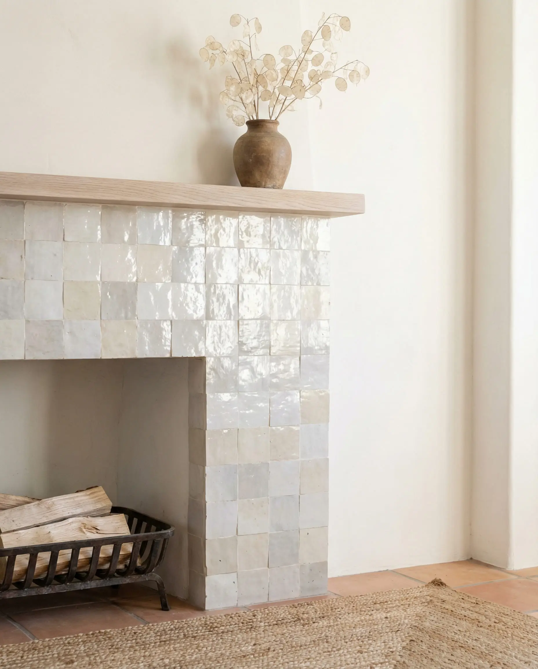 A pearlescent white Zellige tile fireplace surround showing the imperfect, handcrafted texture and glistening glaze.