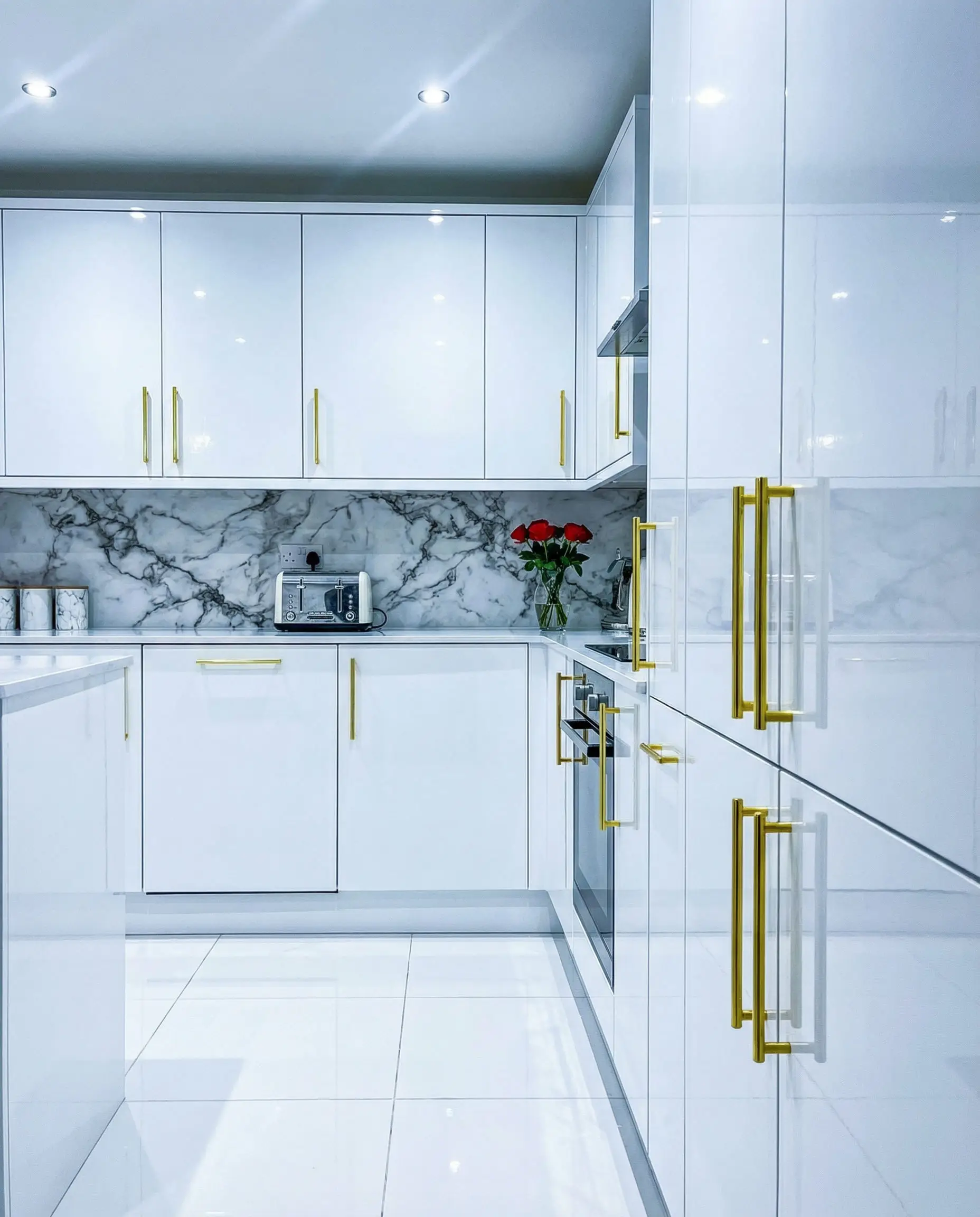 Comparison showing a high-gloss white kitchen with bright yellow gold hardware, representing the older glam trend.