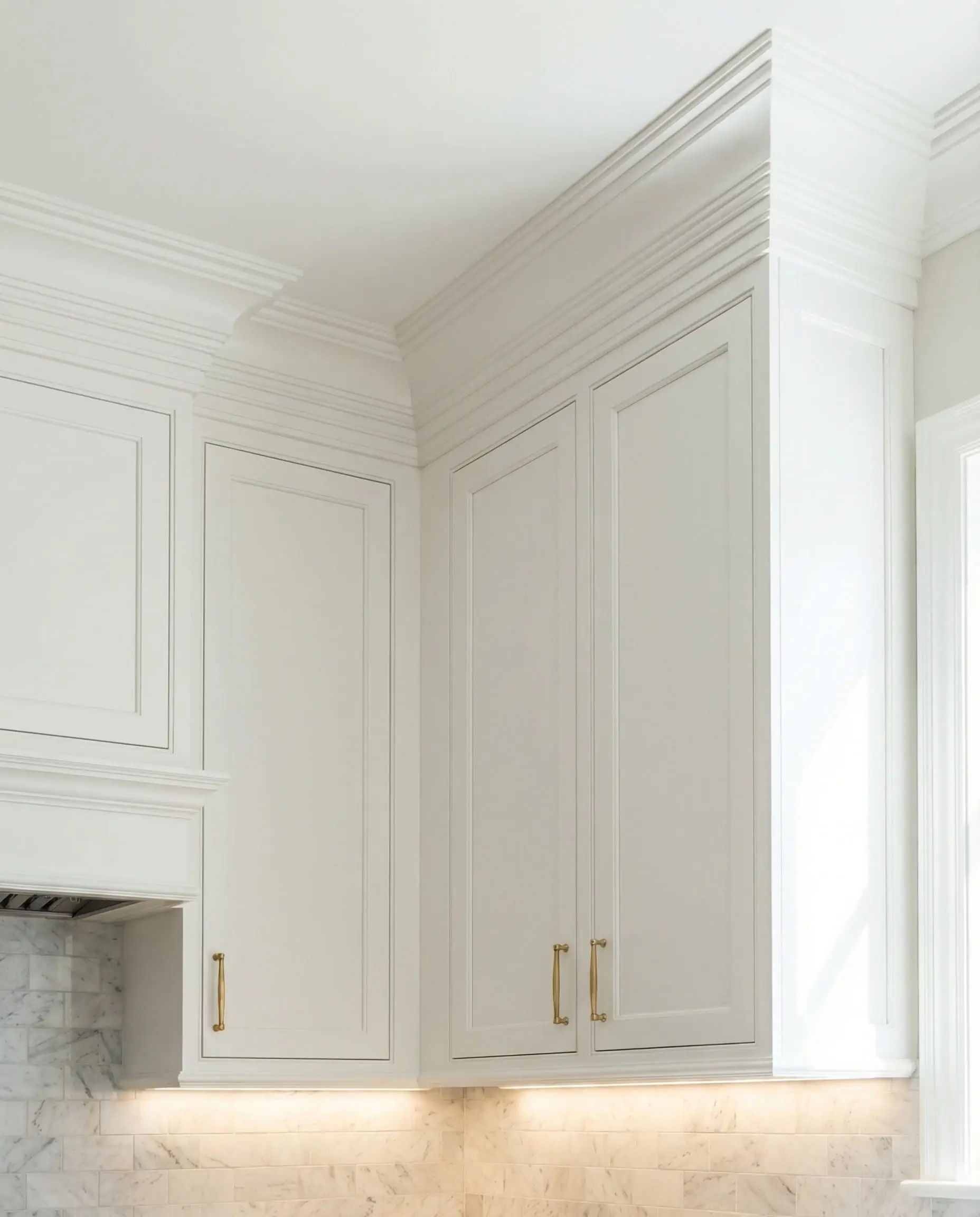 Luxury white kitchen cabinets extending to the ceiling with integrated crown molding to hide the soffit and increase visual height.