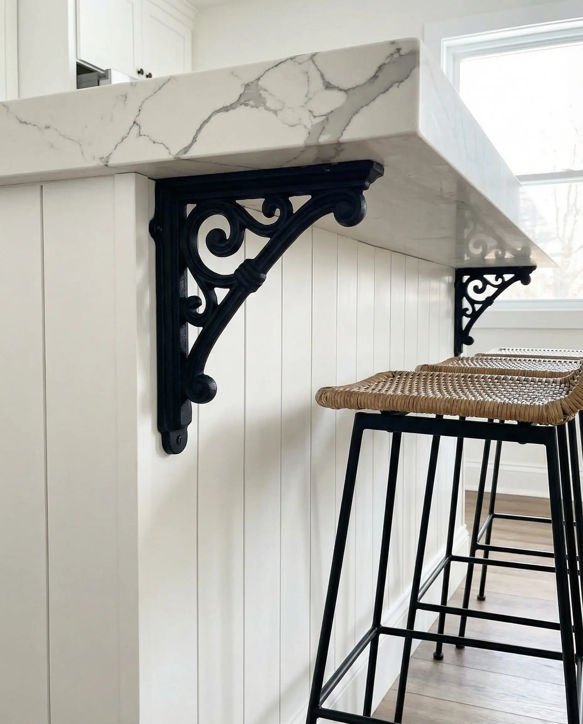 Detail of a white shiplap kitchen island with large matte black iron corbels supporting the quartz countertop overhang.