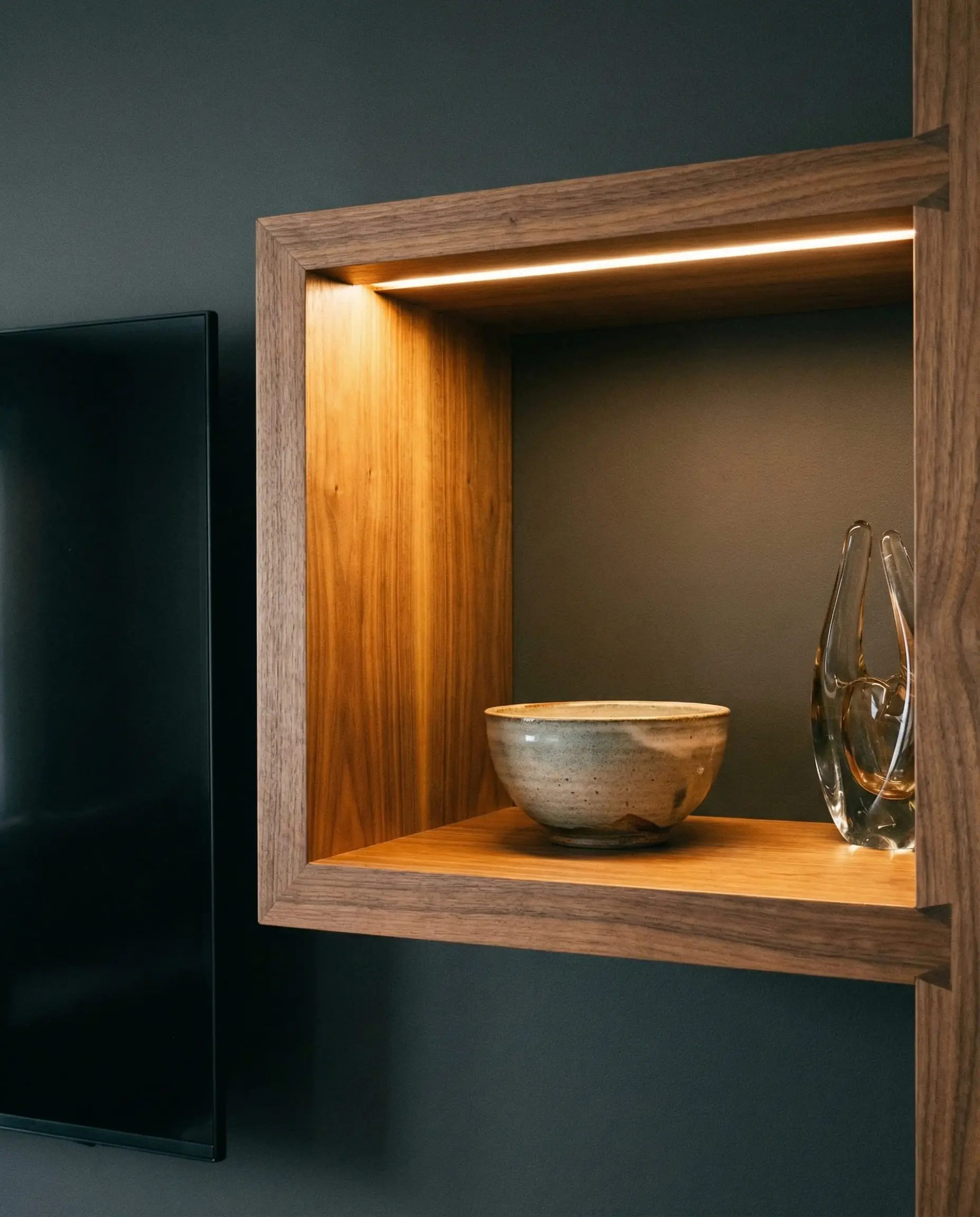 Close-up of recessed LED channel lighting illuminating a walnut shelf next to the TV.