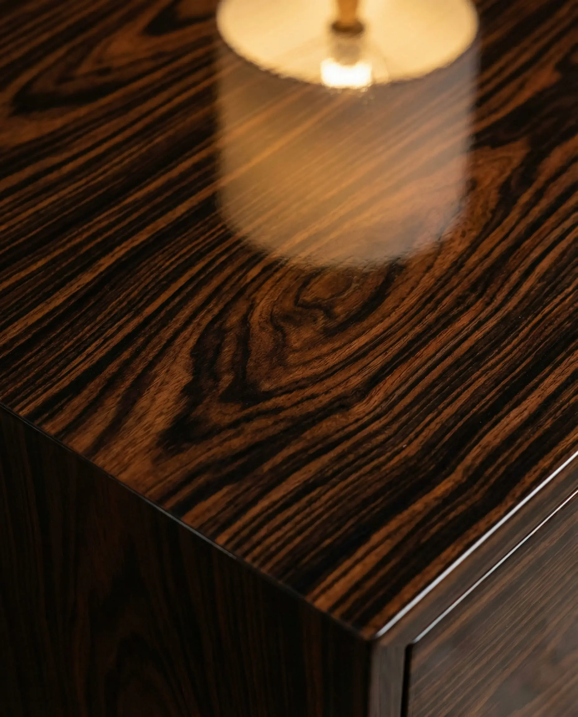 Extreme close-up of Macassar Ebony wood grain with dark brown stripes and a high-gloss lacquer finish.