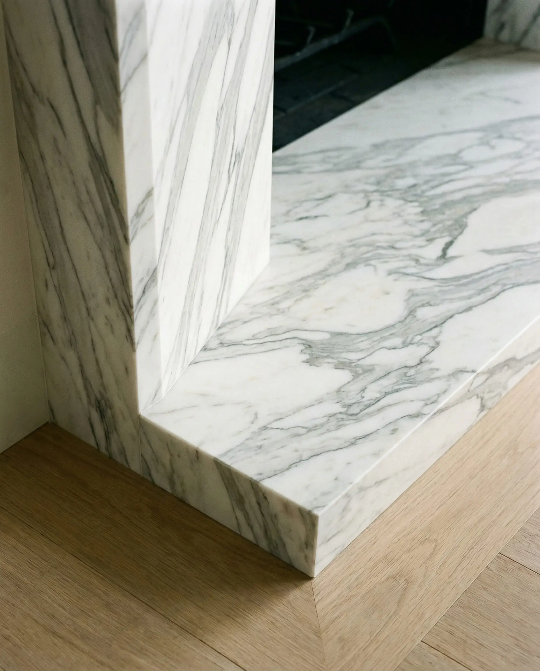 Close-up of a mitered edge on a marble fireplace hearth, showing the "waterfall" effect where veins flow over the edge.