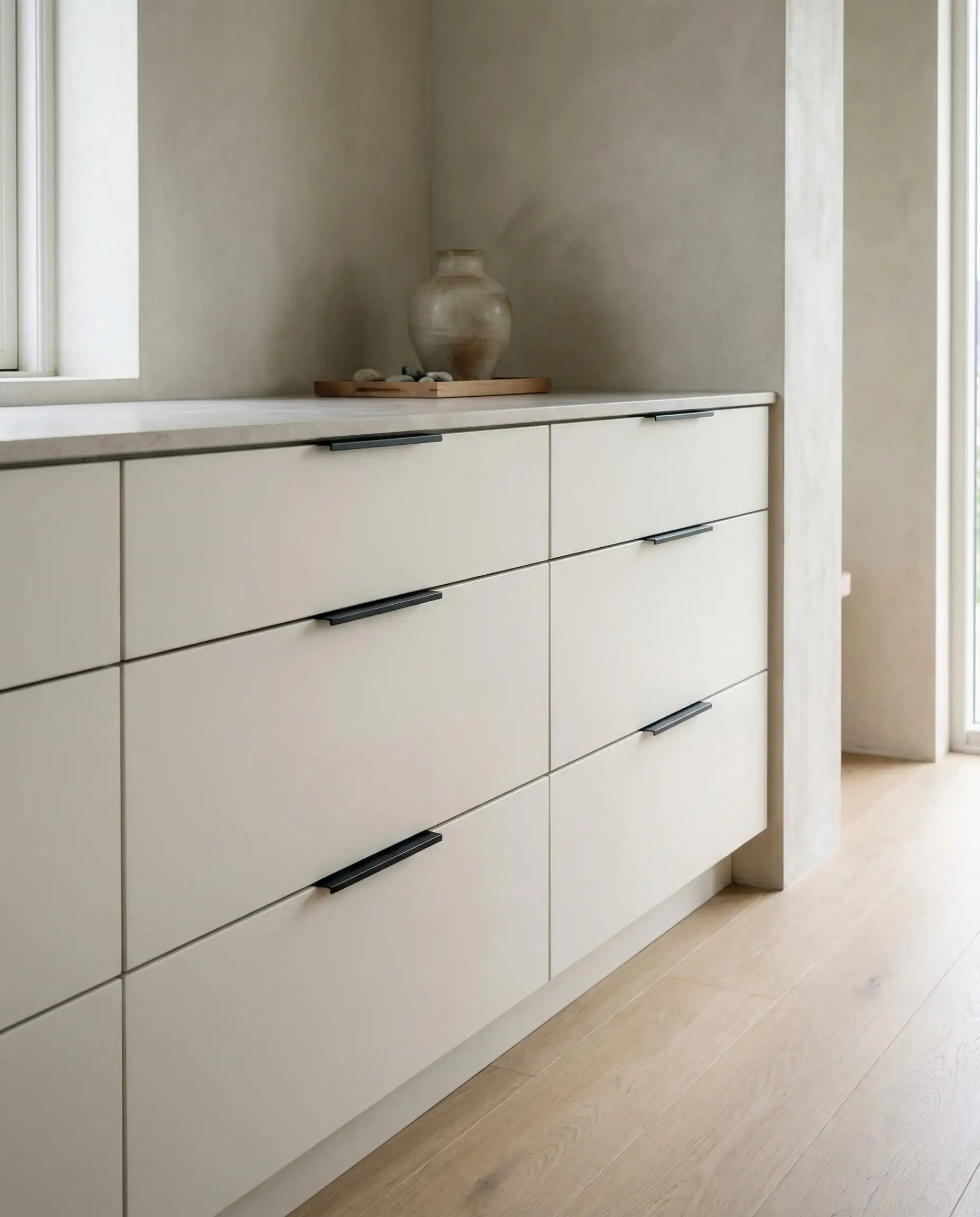 Minimalist drawer detail showing ultra-thin matte black finger tab pulls mounted to the top edge of white drawers.