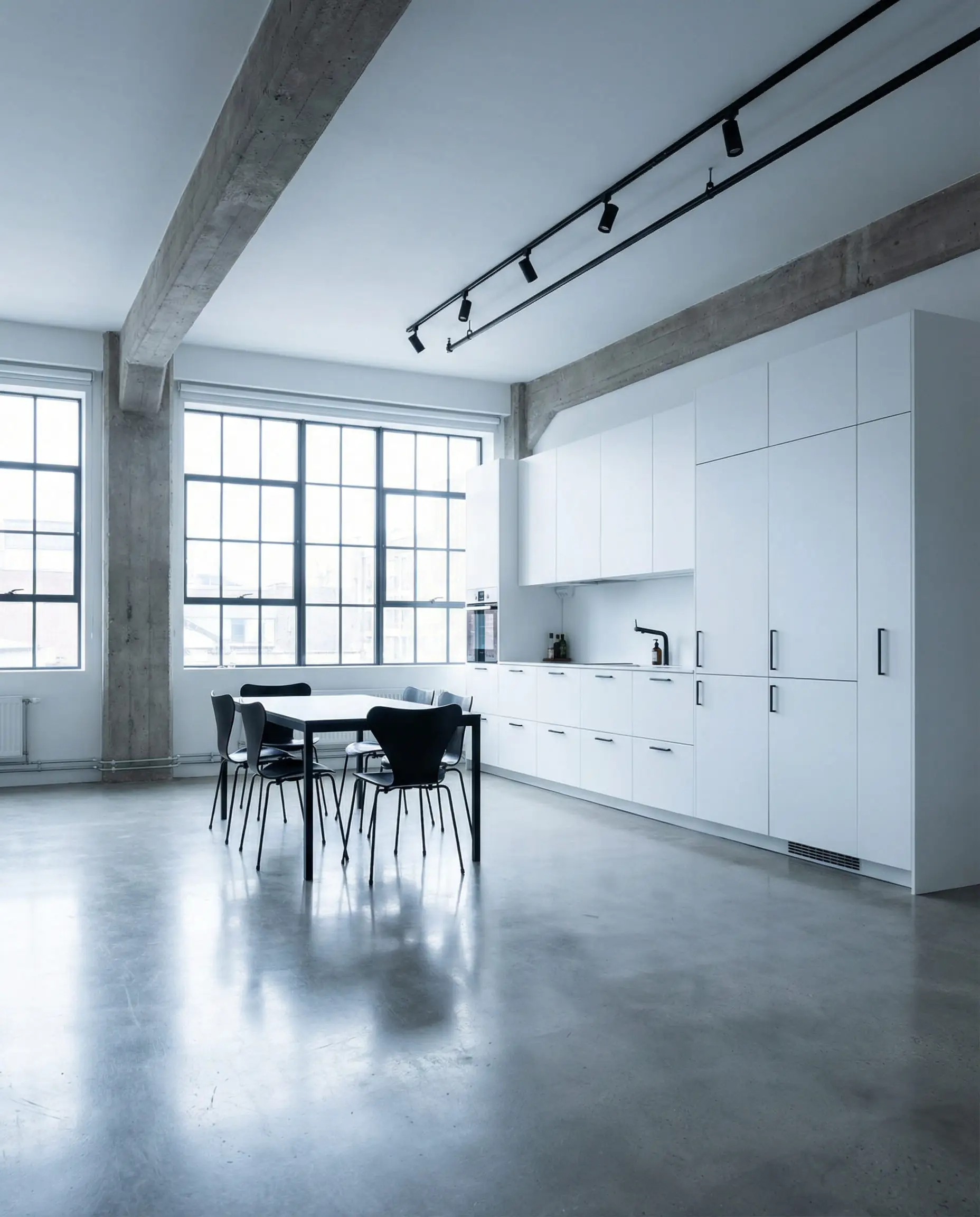 Wide shot of a minimalist white kitchen in a loft with polished concrete floors and black track lighting.