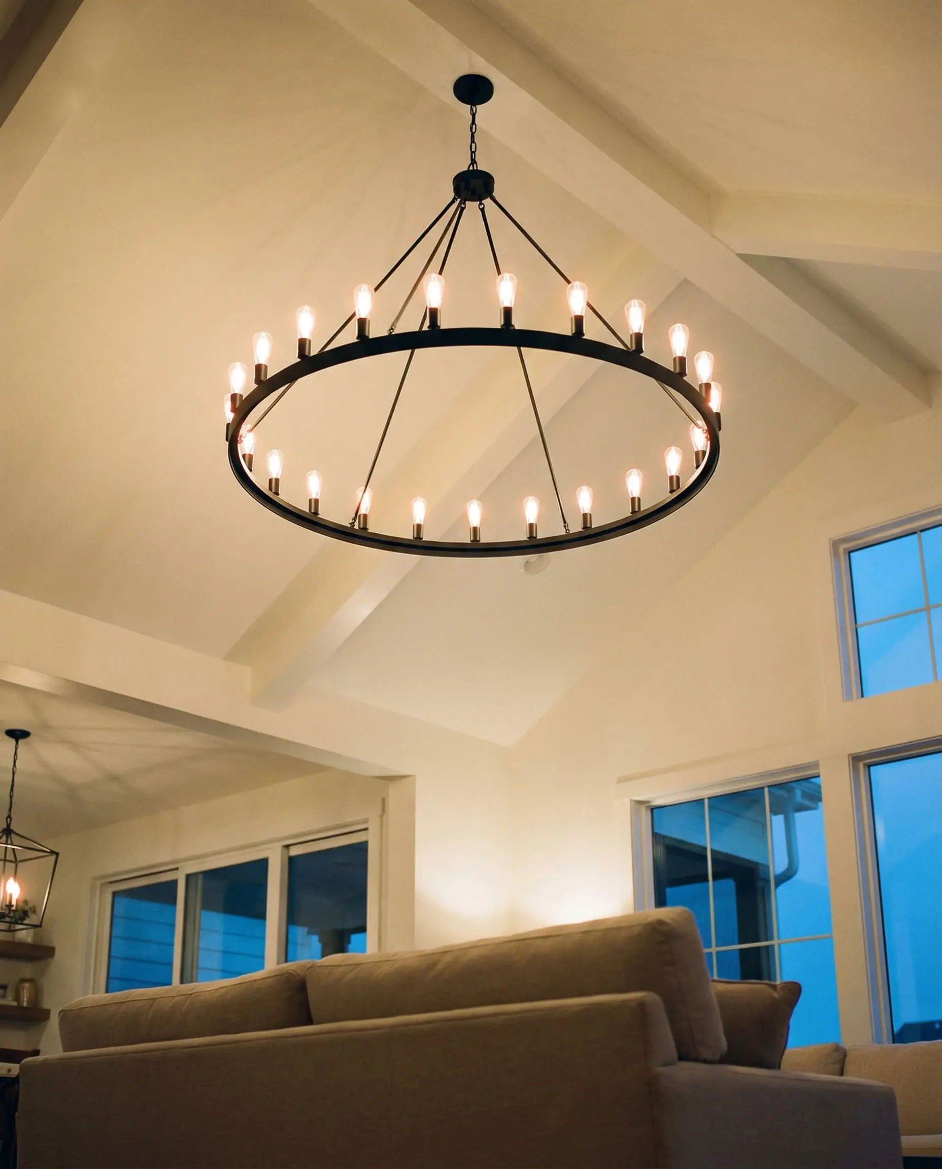 An oversized matte black wrought iron wagon wheel chandelier hangs from a vaulted ceiling, highlighting modern farmhouse decor.