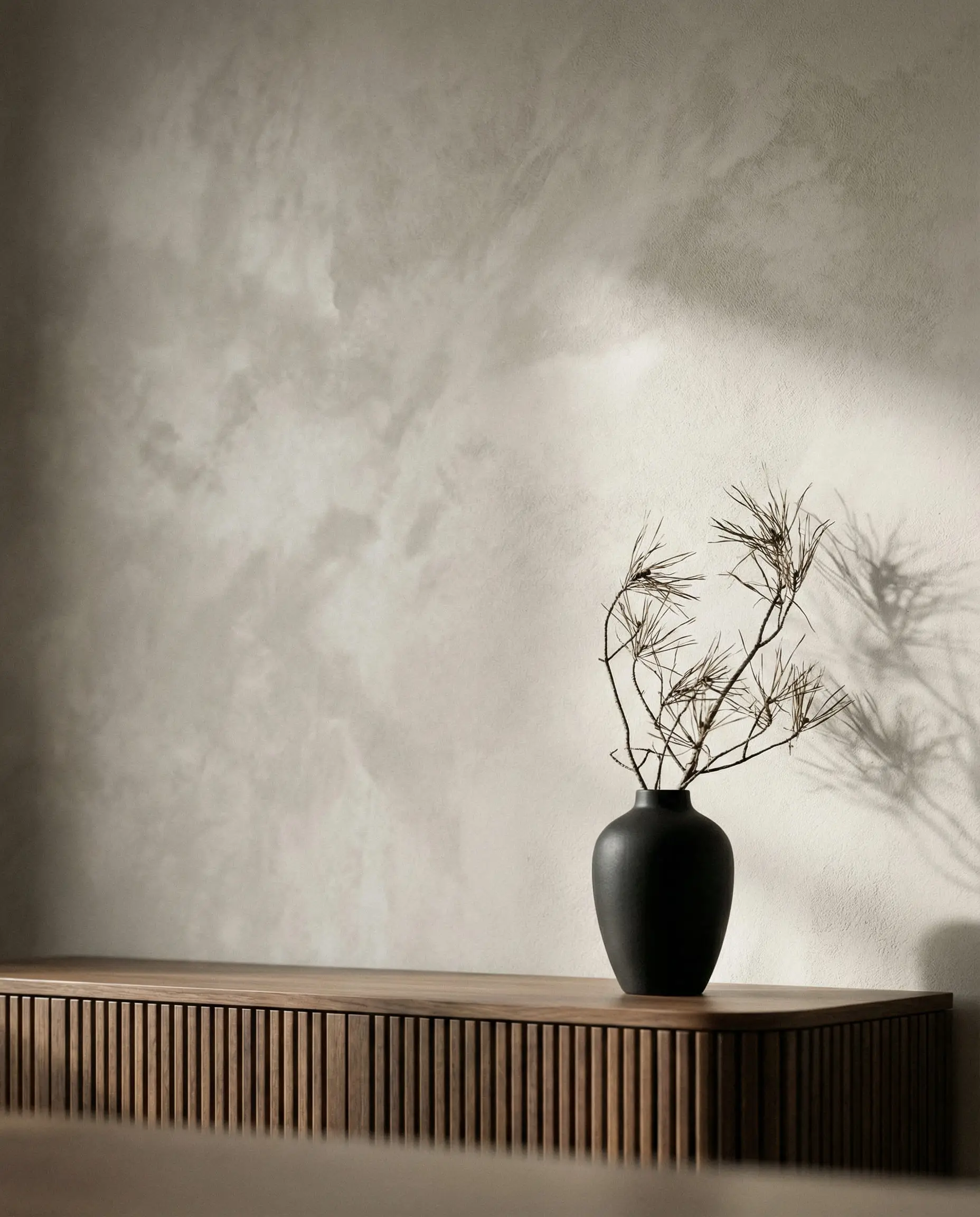 Close-up detail of mushroom taupe limewash paint texture on a dining room wall with shadow play from dried branches in a Japandi setting.
