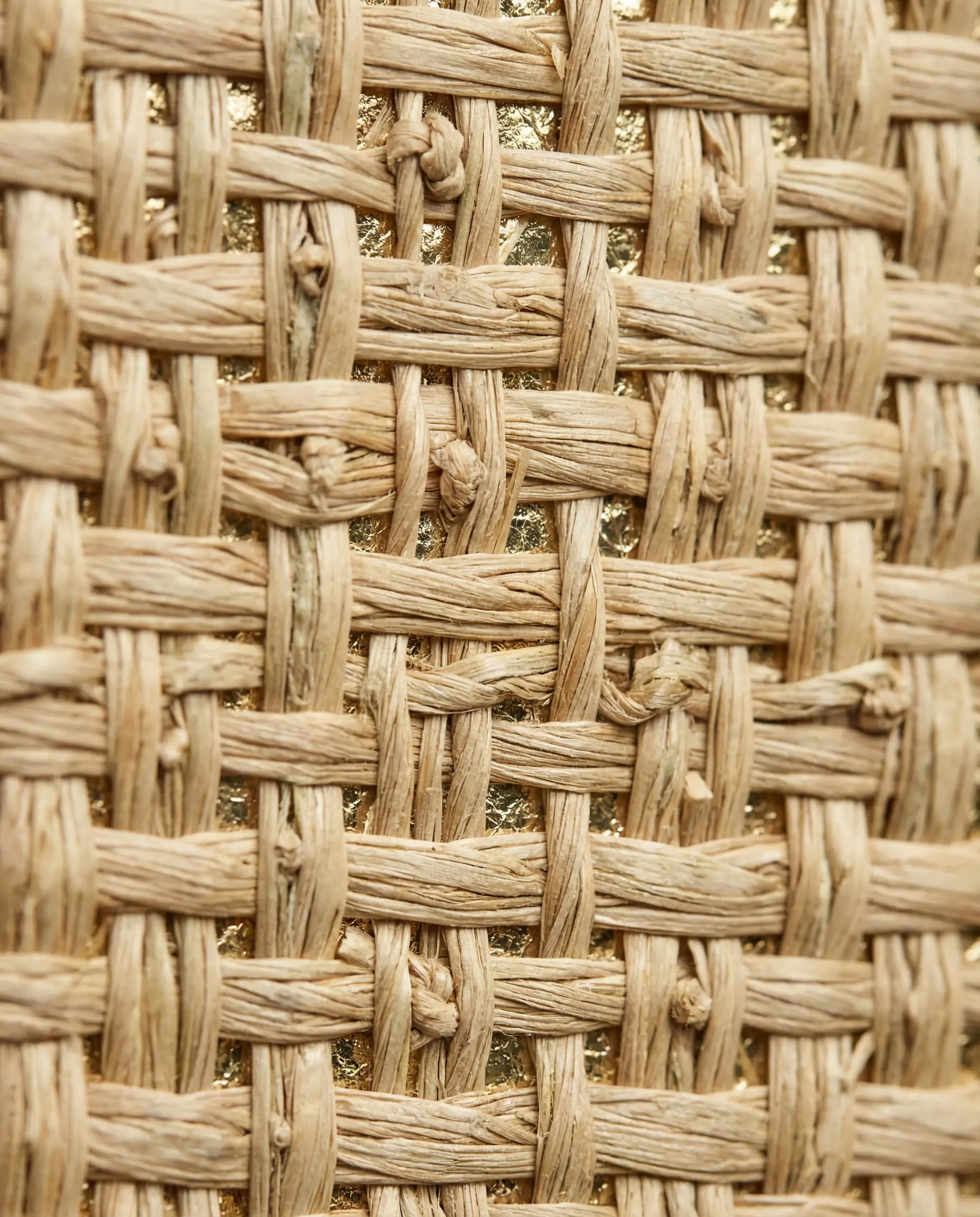 Macro close-up of natural seagrass wallpaper showing woven fibers and metallic gold backing texture.