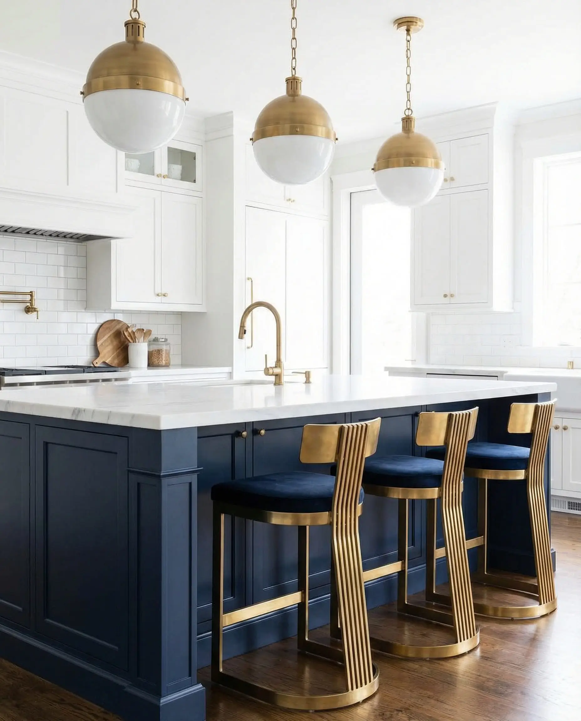 Detail of a deep navy blue kitchen island paired with brass Art Deco bar stools and pendant lighting.