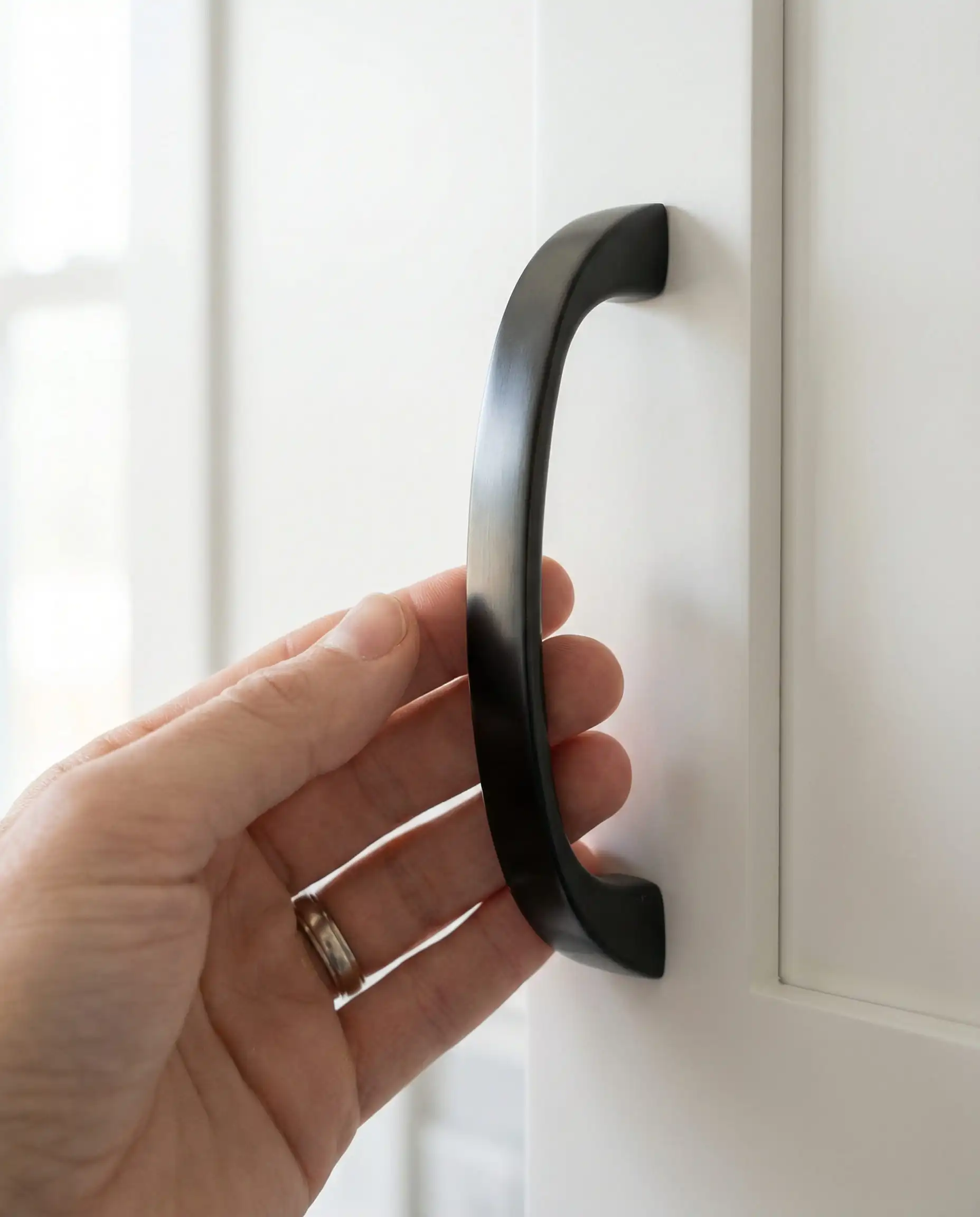 Close up of a hand reaching for an oil-rubbed bronze cabinet pull showing a subtle sheen that resists fingerprints.