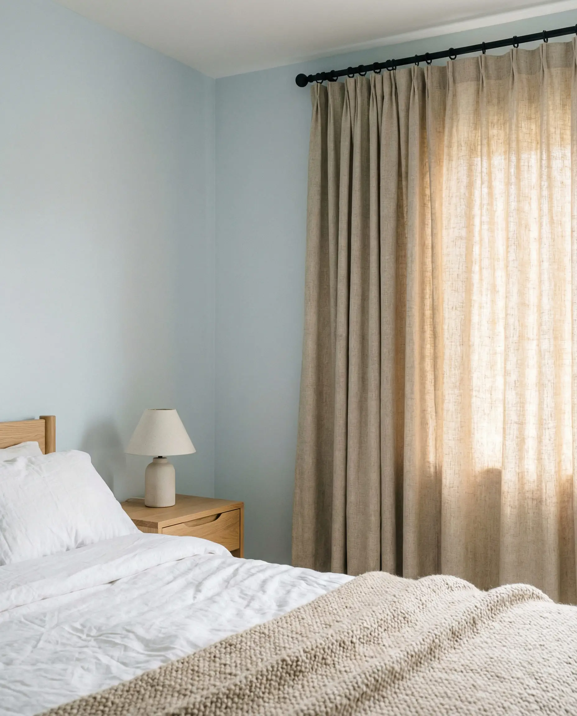 Serene organic modern bedroom with pale blue walls and textured oatmeal linen curtains.