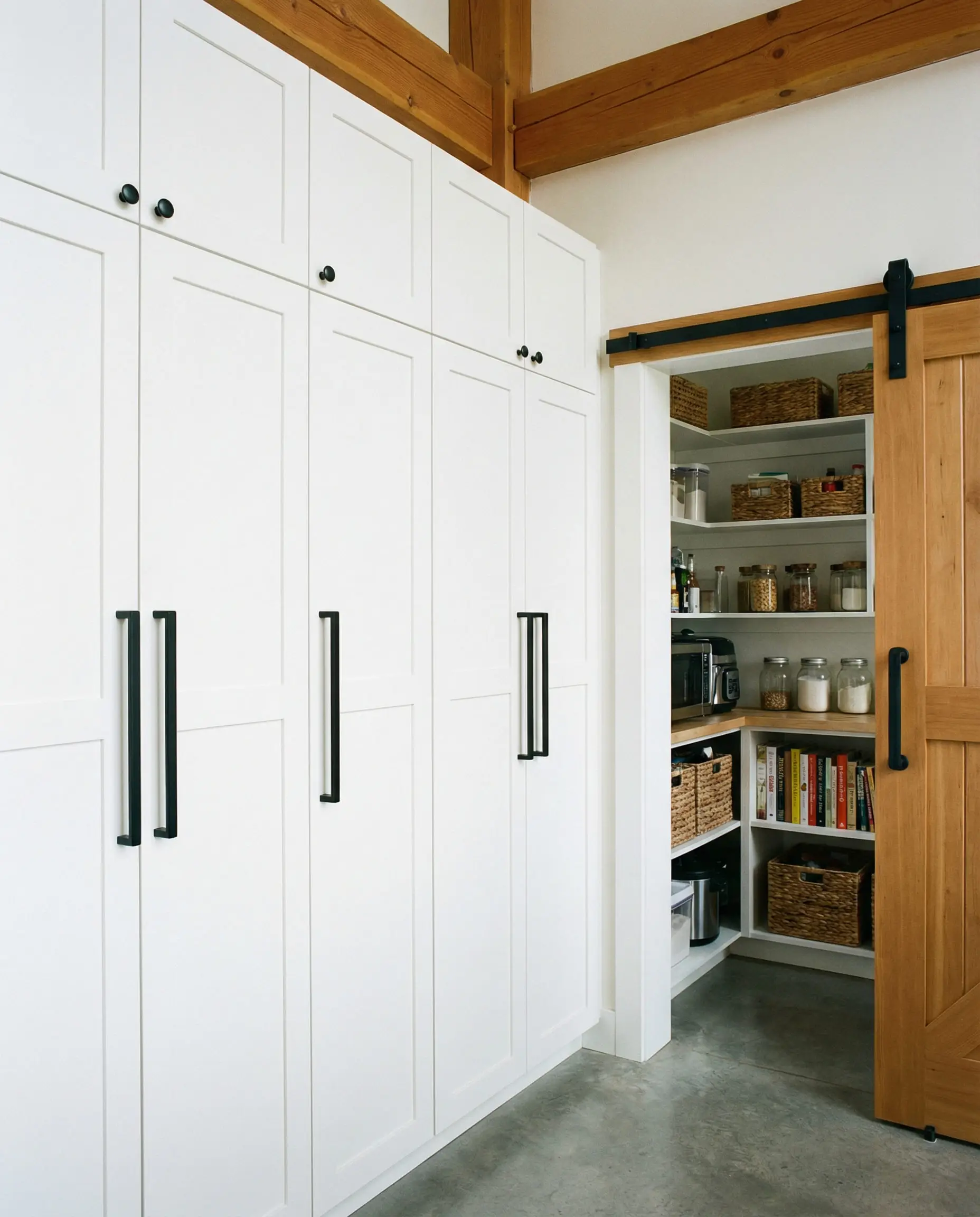 Floor-to-ceiling white pantry cabinet wall featuring oversized extra-long matte black bar pulls for a dramatic look.