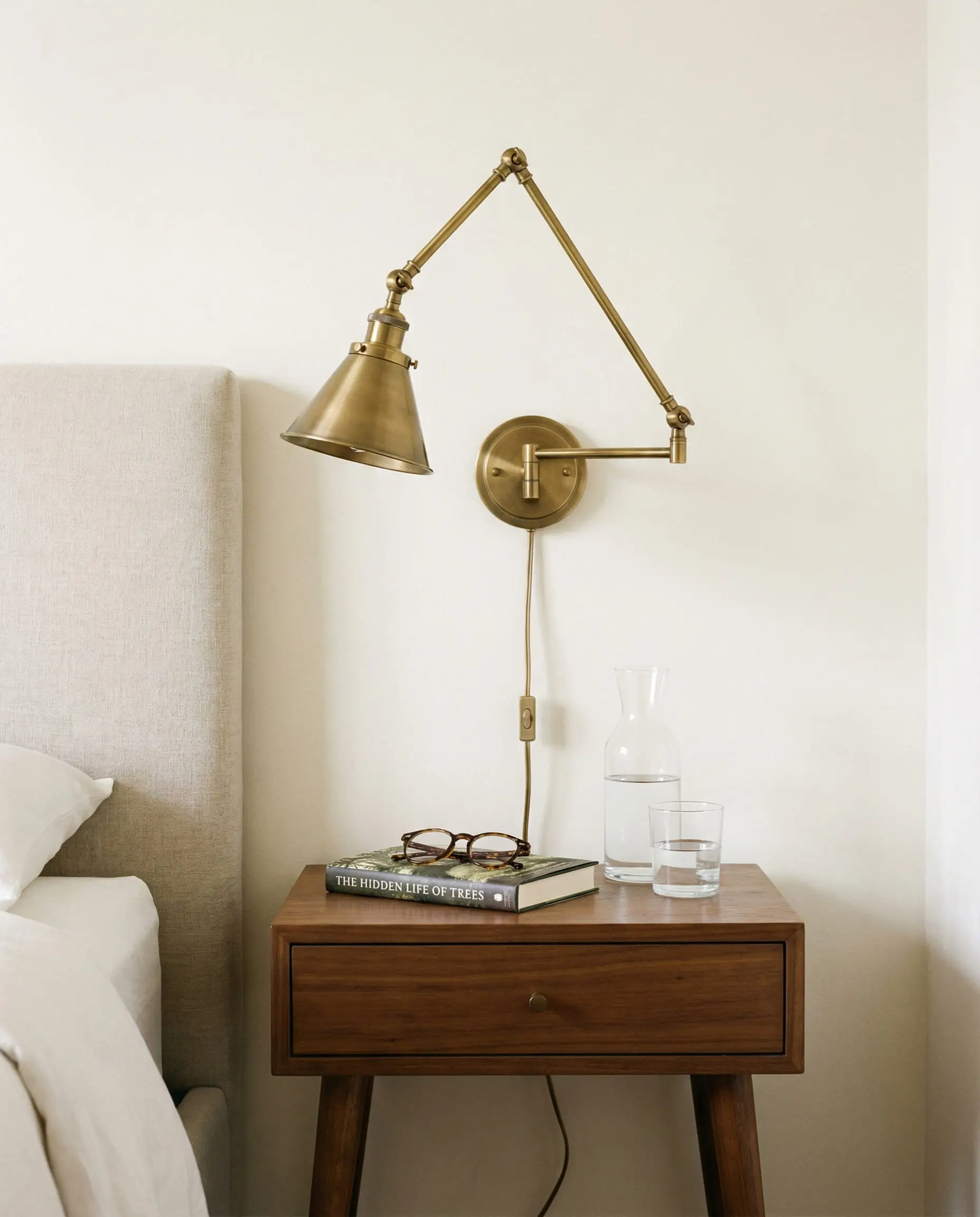 Brass plug-in wall sconce mounted next to a bed above a walnut nightstand.