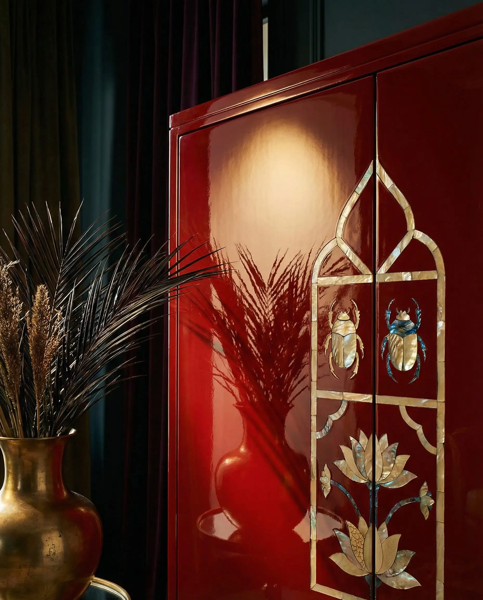 Macro shot of a high-gloss red lacquer cabinet with mother-of-pearl Egyptian revival inlays and a gold vase reflection.