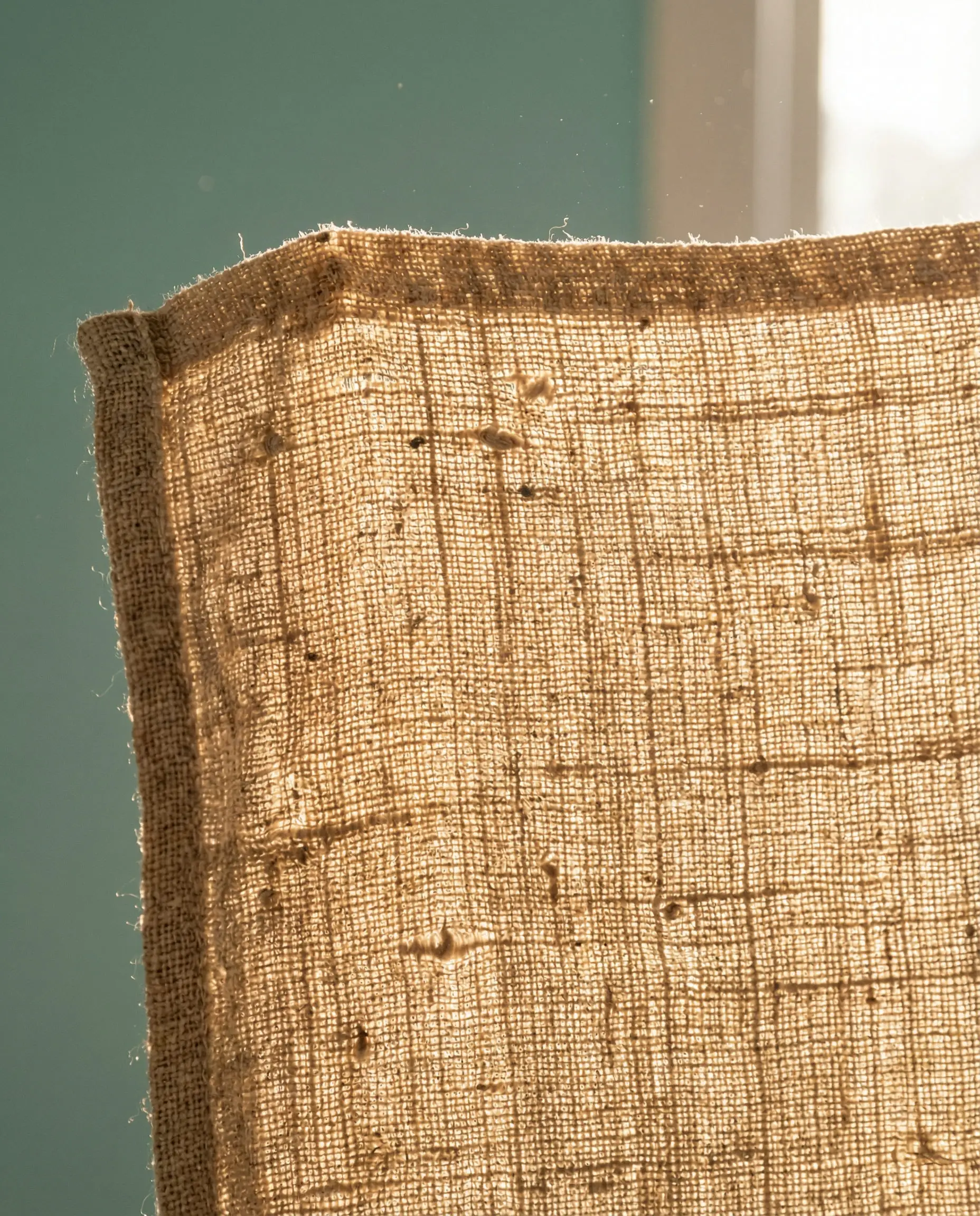 Detail shot of rough tan linen fabric weave against a teal wall.