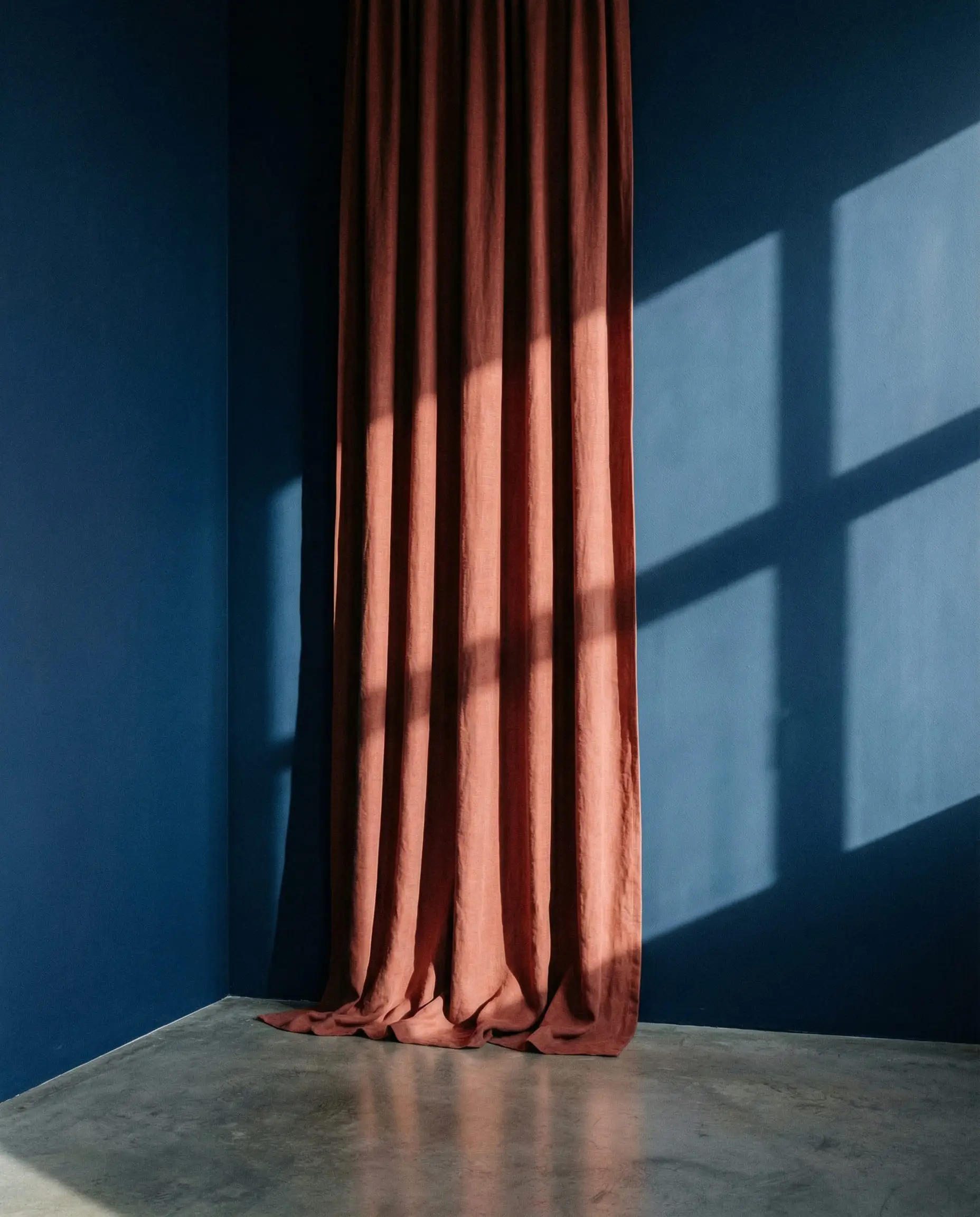 Minimalist dark royal blue wall with a single panel of clay-colored linen curtain.