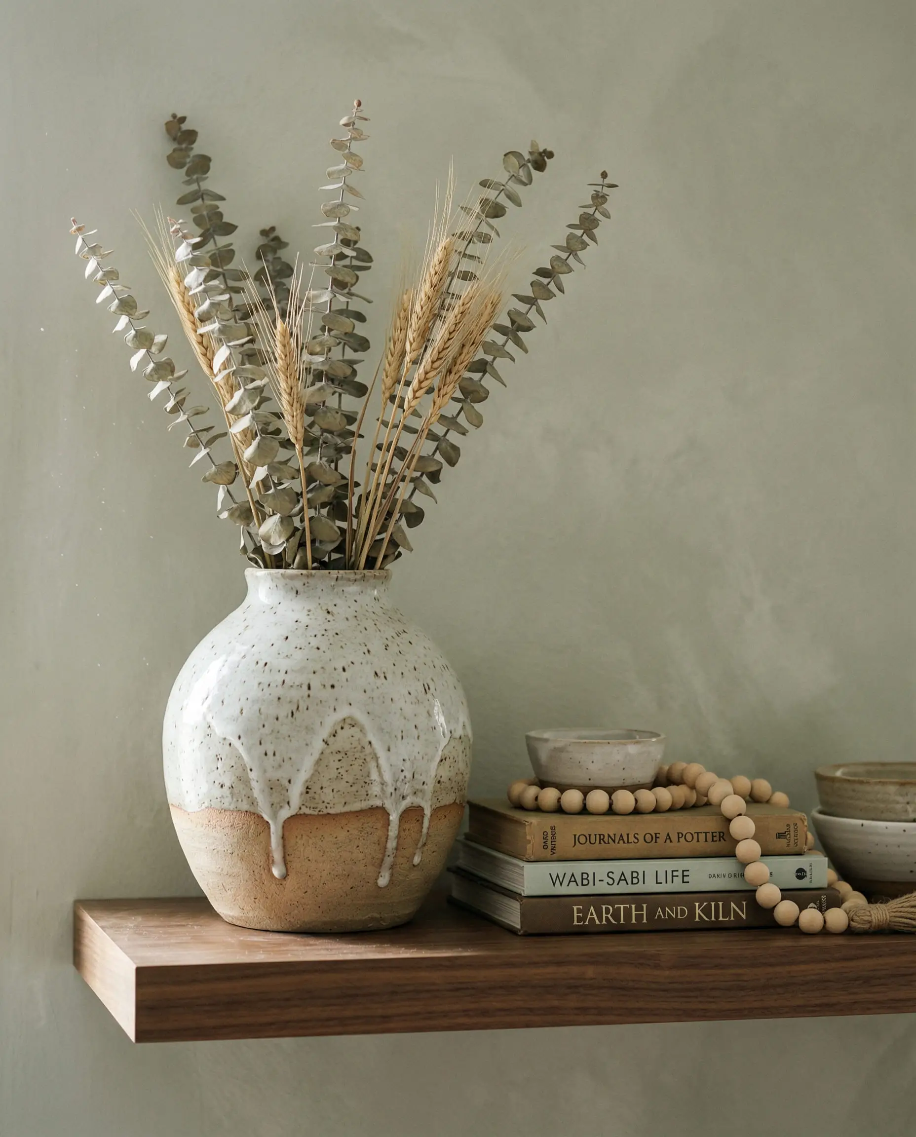 Still life of a hand-thrown ceramic vase with dried eucalyptus on a floating walnut shelf.