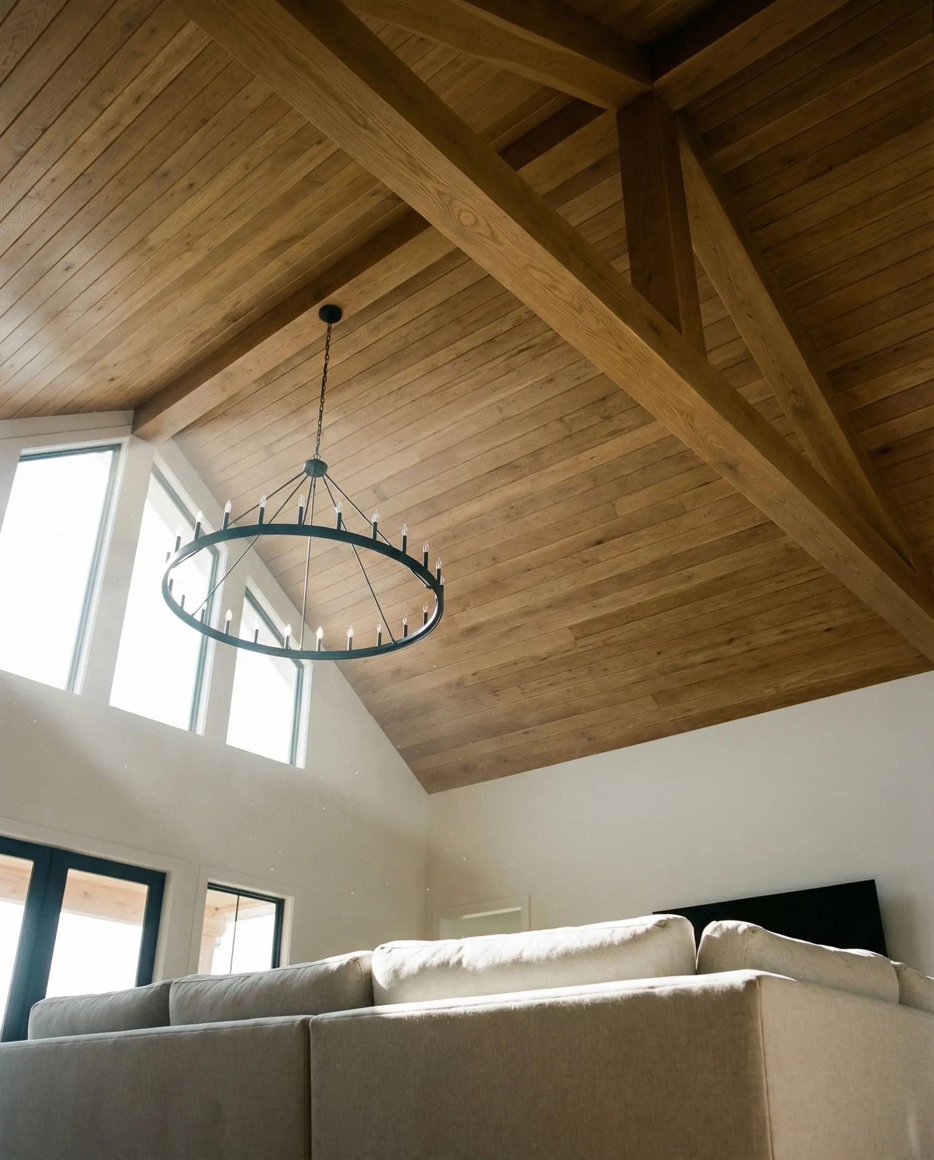 Soaring vaulted ceilings showcase warm oak architectural features and a black wagon wheel chandelier in a rustic modern space.