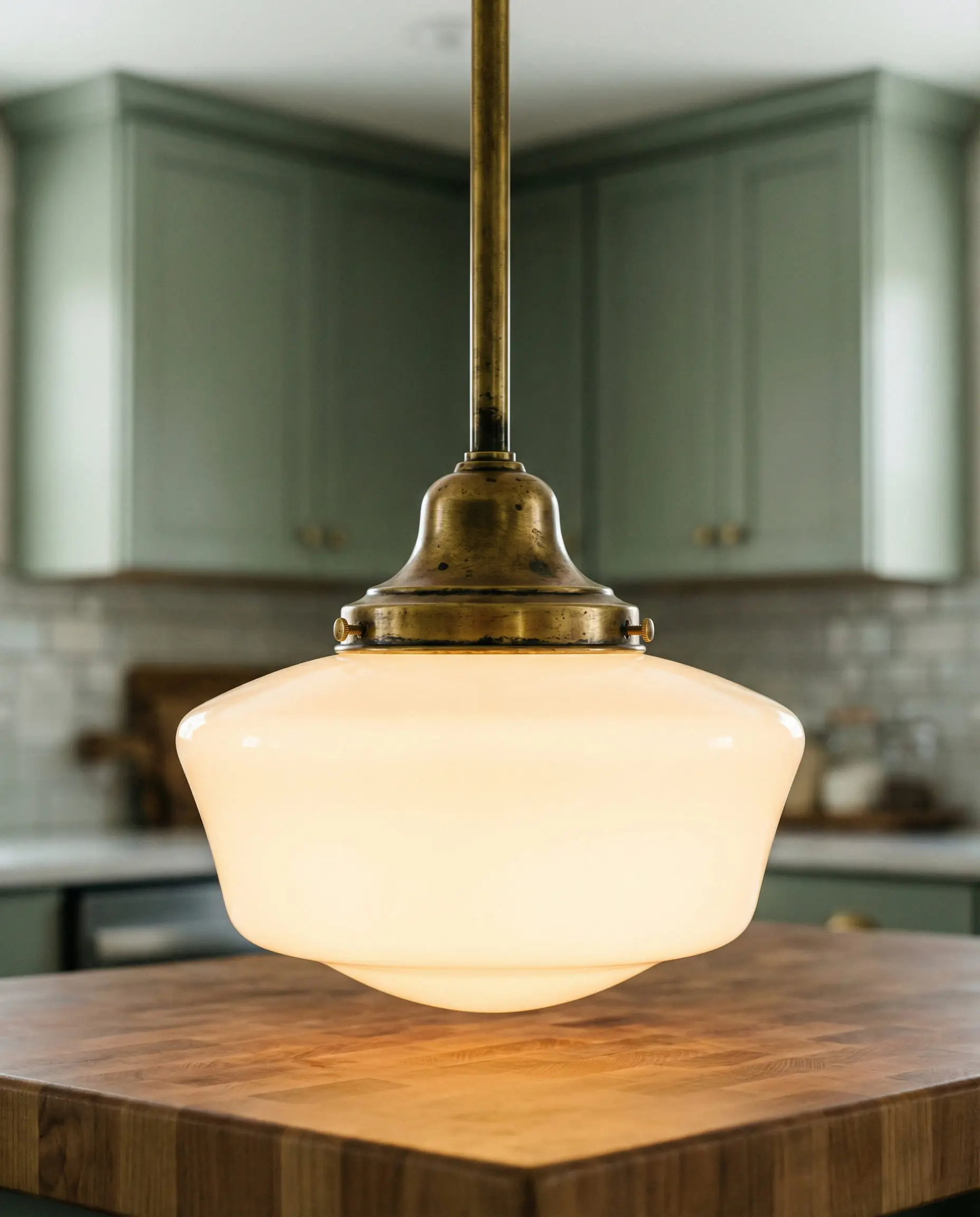 Vintage-style schoolhouse glass pendant light with an unlacquered brass fitter hanging over a kitchen island.