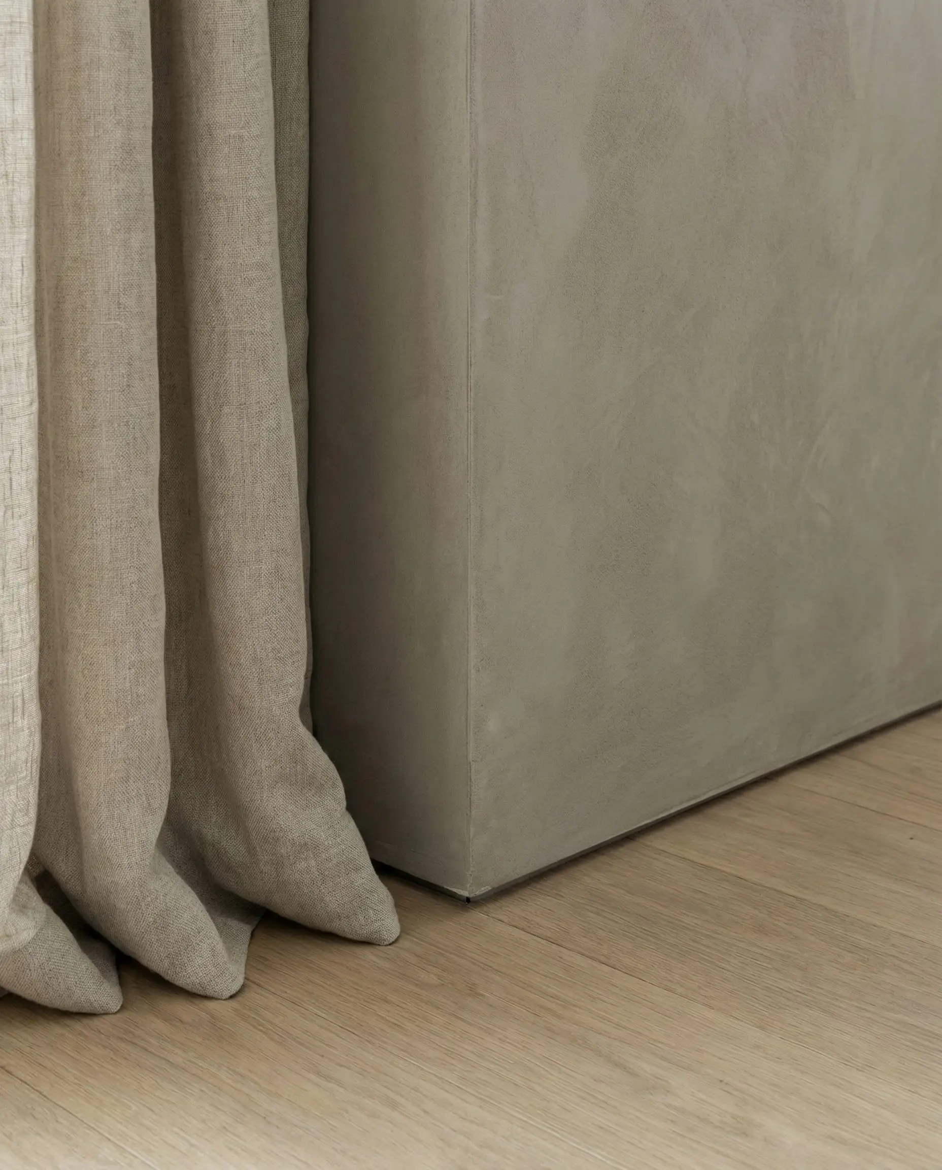 Architectural detail of a microcement wall meeting an oak floor with a shadow gap and no baseboard, featuring linen curtains.