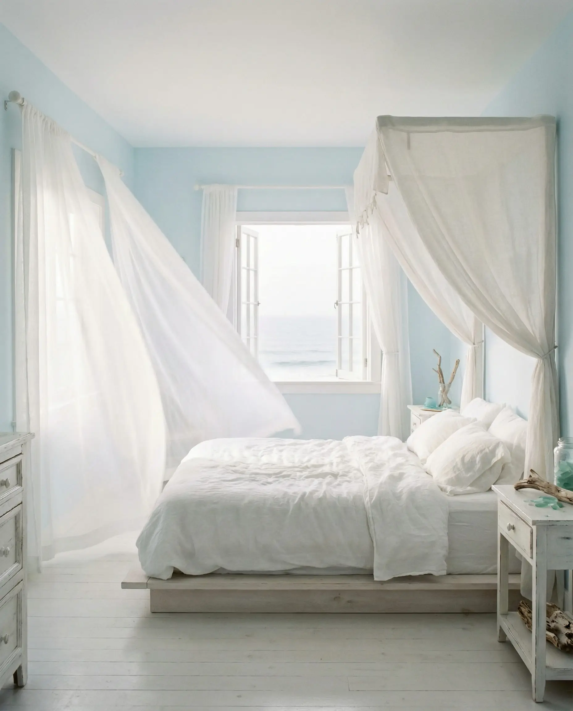 Airy coastal bedroom with sky blue walls and sheer white voile curtains blowing in the breeze.