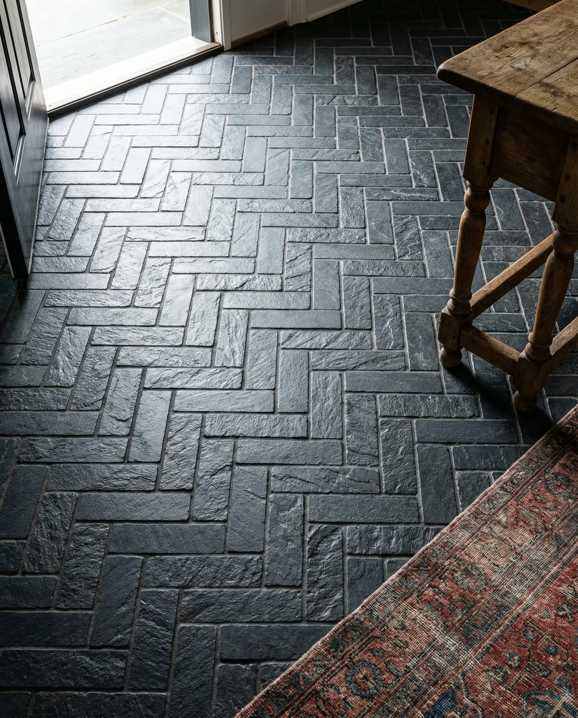 Dark slate tiles laid in a herringbone pattern in a foyer with a vintage runner rug.