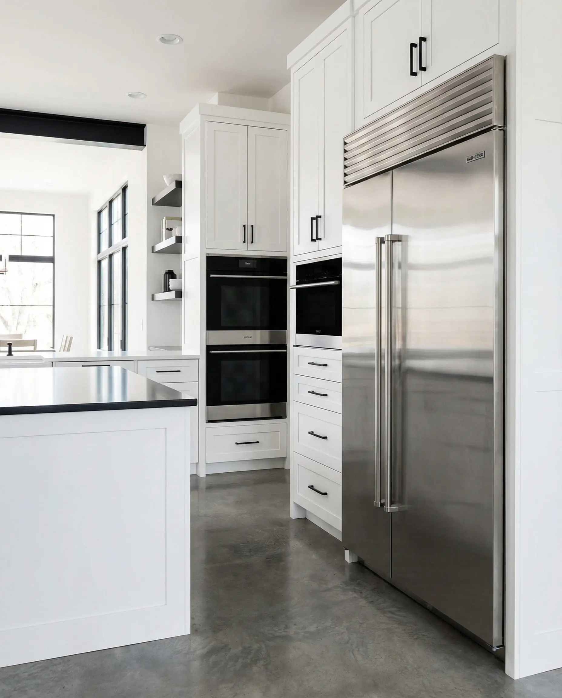 Wide shot showing professional stainless steel appliances integrated into white cabinetry with black hardware.