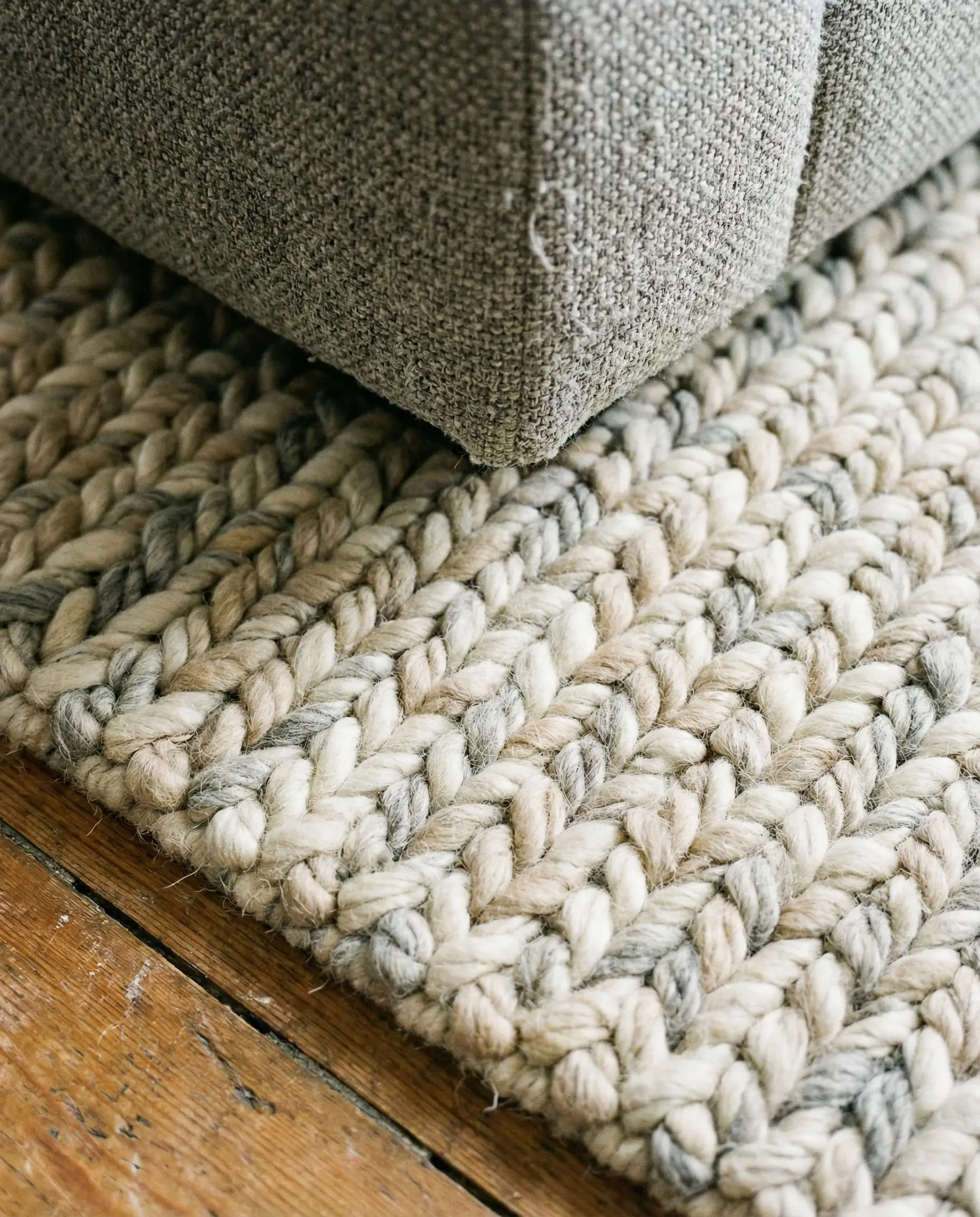 Close-up detail of a chunky hand-woven cream and beige wool rug placed underneath a textured grey sofa.