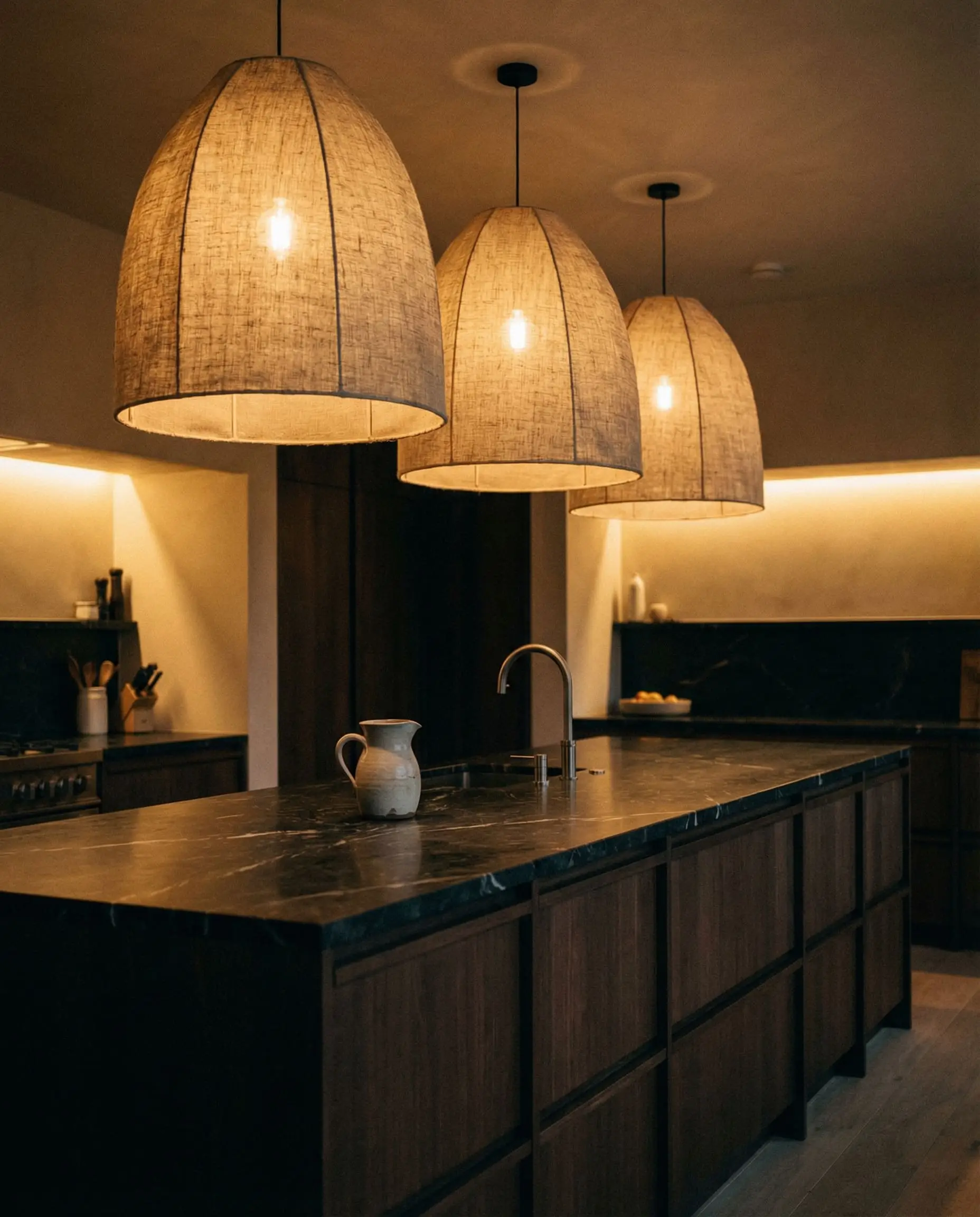 Oversized draped heavy linen pendants provide traditional softness above a sleek modern kitchen island.