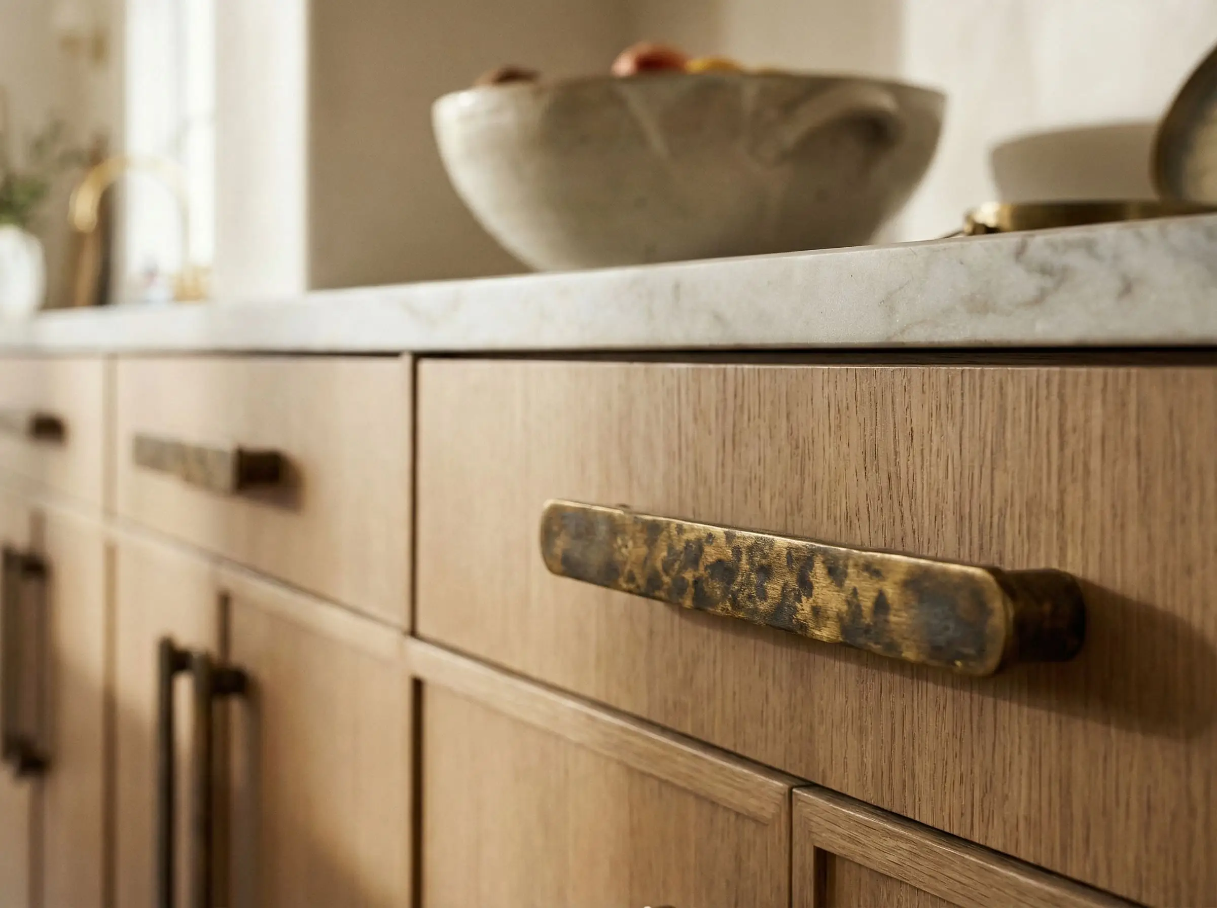 An ornate unlacquered brass pull with dark patina is mounted directly onto a modern flat-panel white oak drawer.