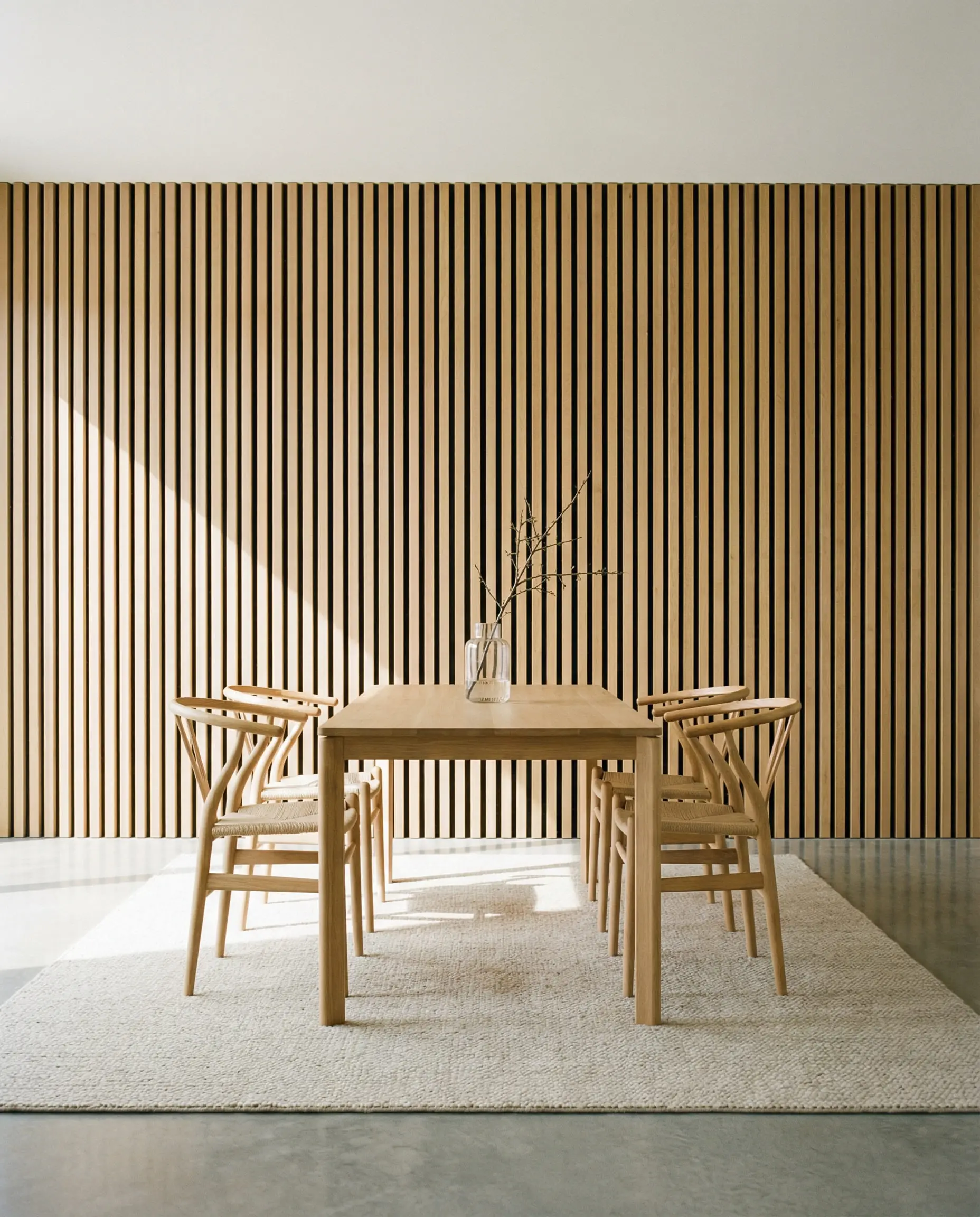 Japandi-style dining room with a floor-to-ceiling vertical white oak wood slat accent wall and Hans Wegner Wishbone chairs.
