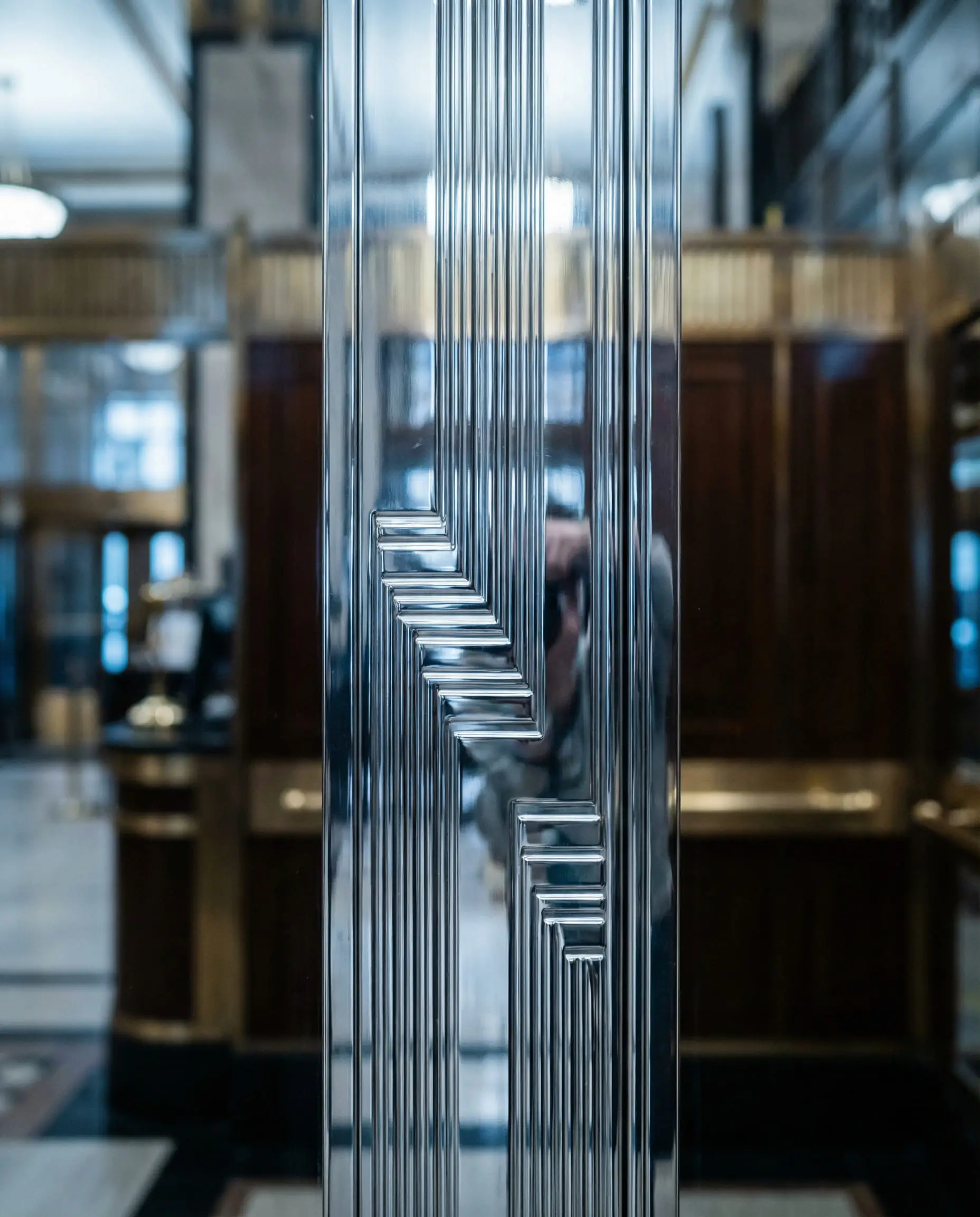 Close-up of polished chrome elevator doors featuring sharp geometric industrial patterns typical of the 1920s Machine Age aesthetic.