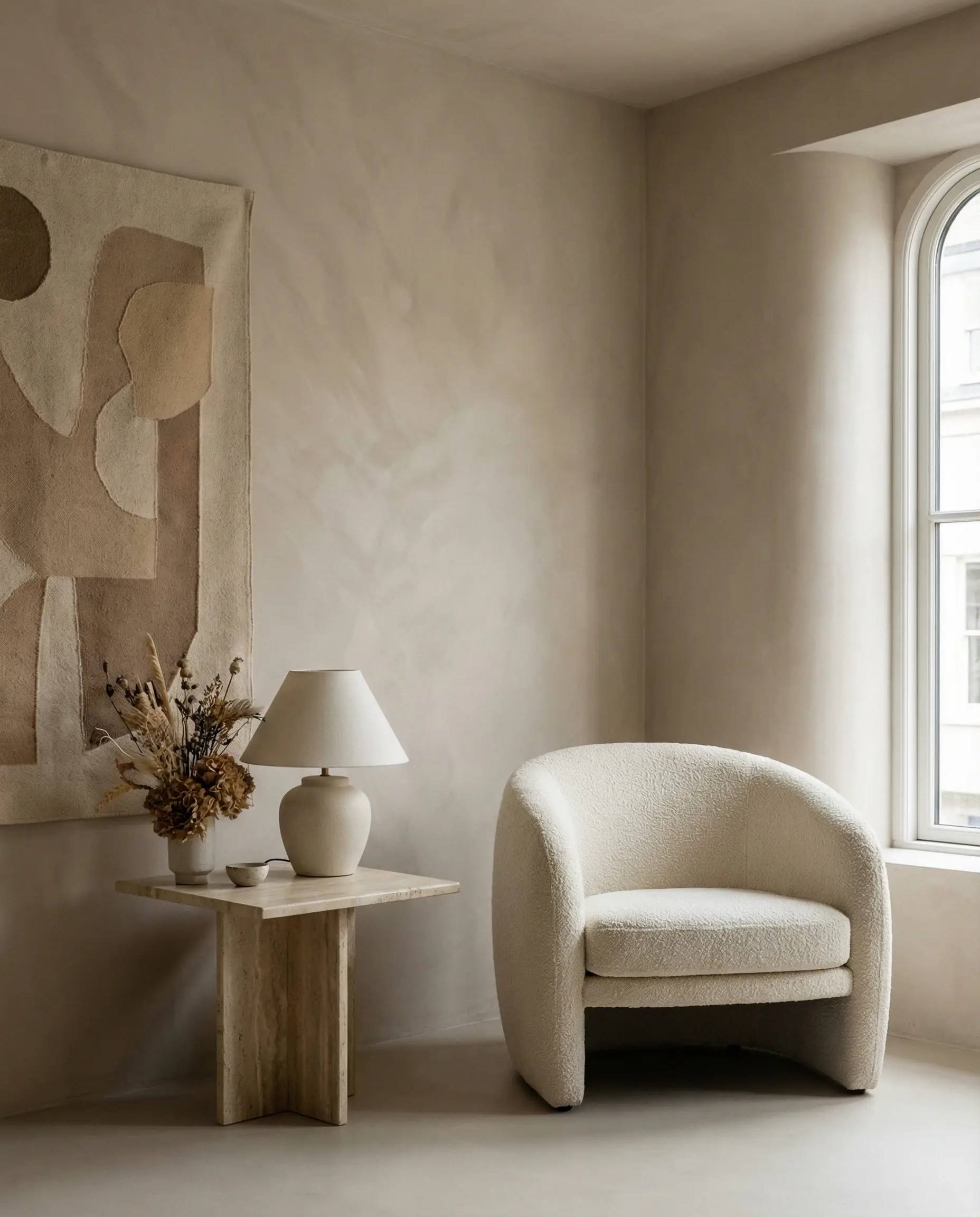 Vertical shot of a modern living room corner with matte mushroom-colored lime wash walls and a cream bouclé armchair.