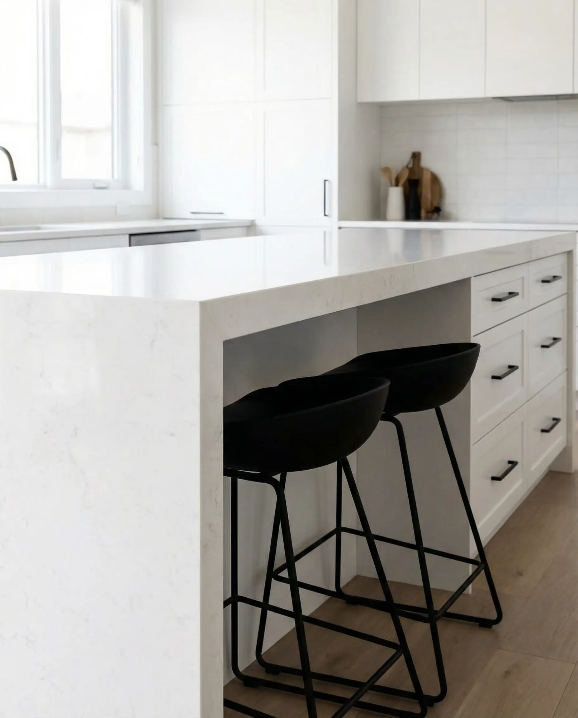 White quartz waterfall island with matte black wire-frame bar stools tucked underneath.