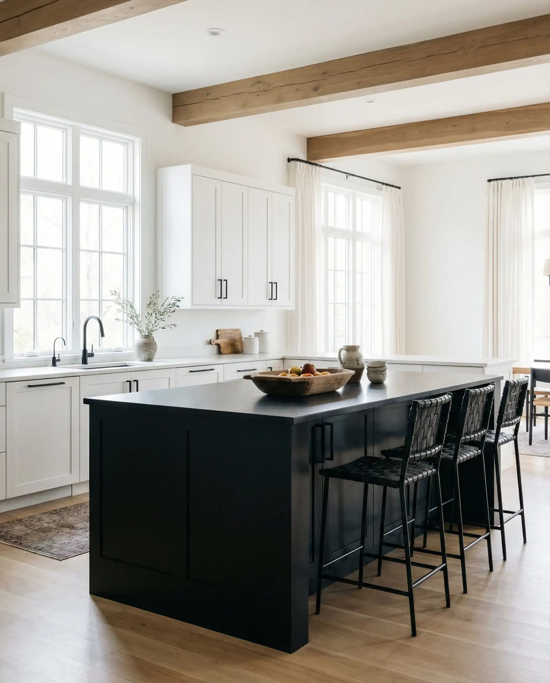 Wide shot of a white perimeter kitchen anchored by a large matte black island with black hardware.