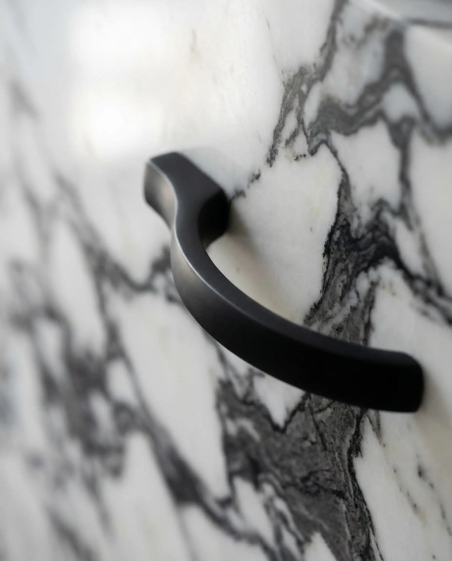 Macro shot showing how matte black cabinet hardware picks up the dark grey veining in Calacatta marble.