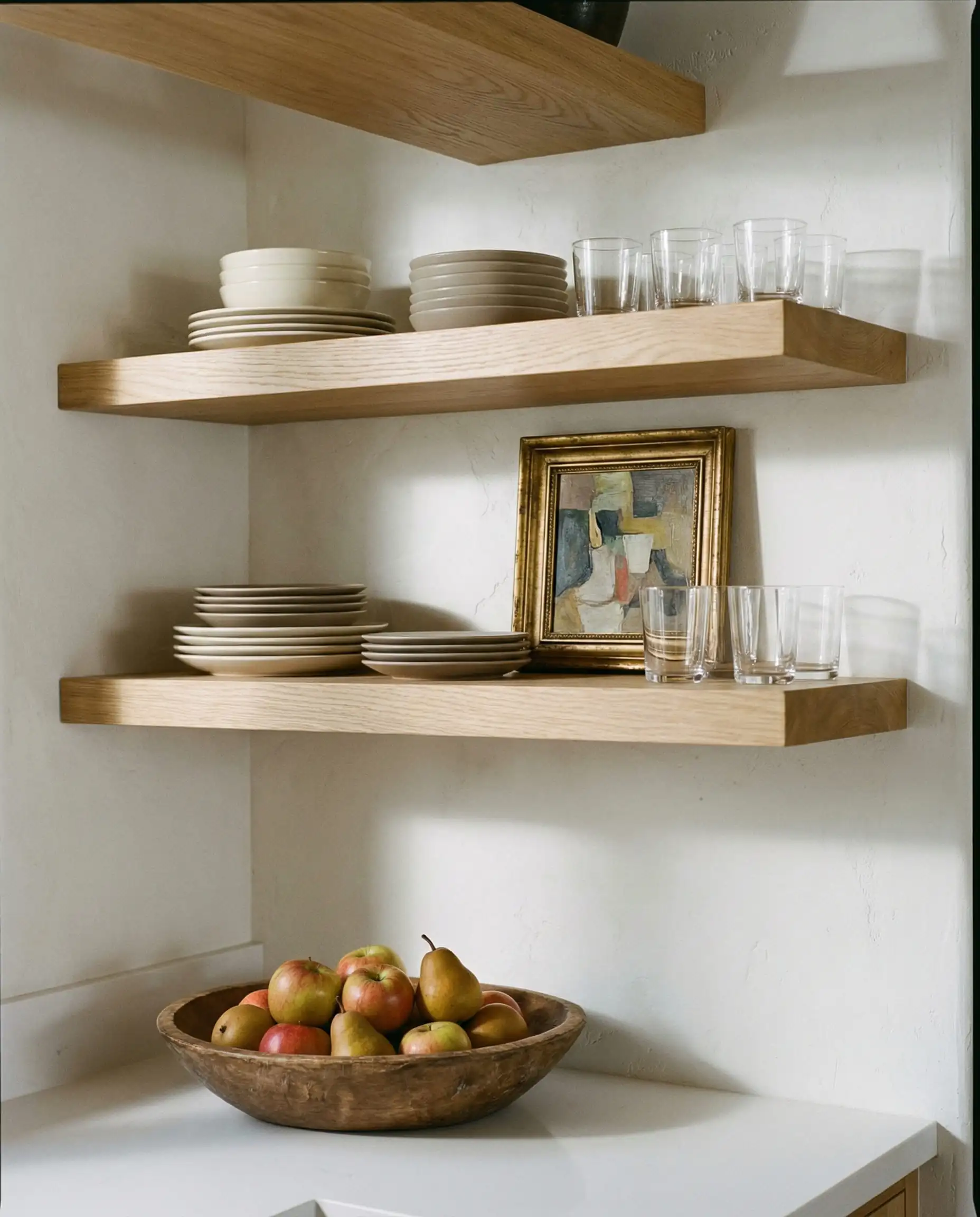 White oak floating shelves on a white plaster wall styled with ceramics and gold-framed art.