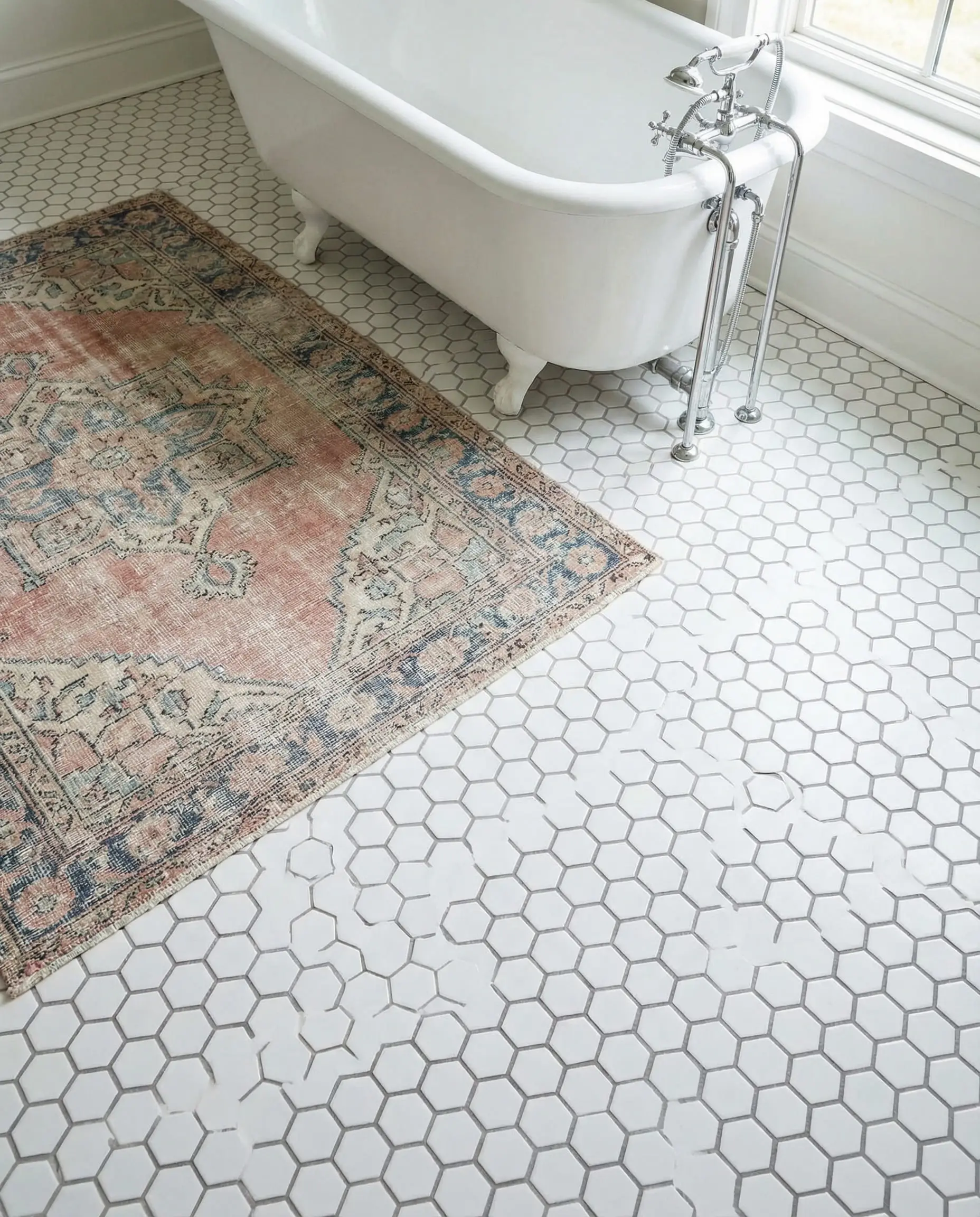 Bathroom floor featuring white hexagonal penny tiles with grey grout and a vintage rug.