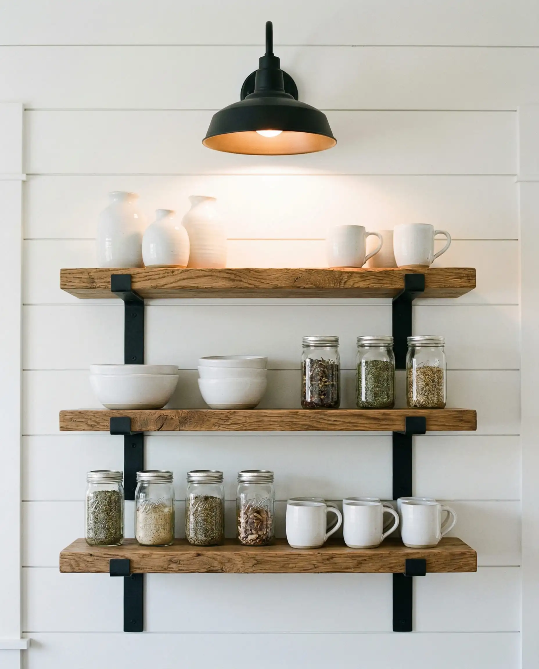 Vertical detail showing white shiplap walls with open white oak shelving supported by heavy-duty matte black metal brackets.