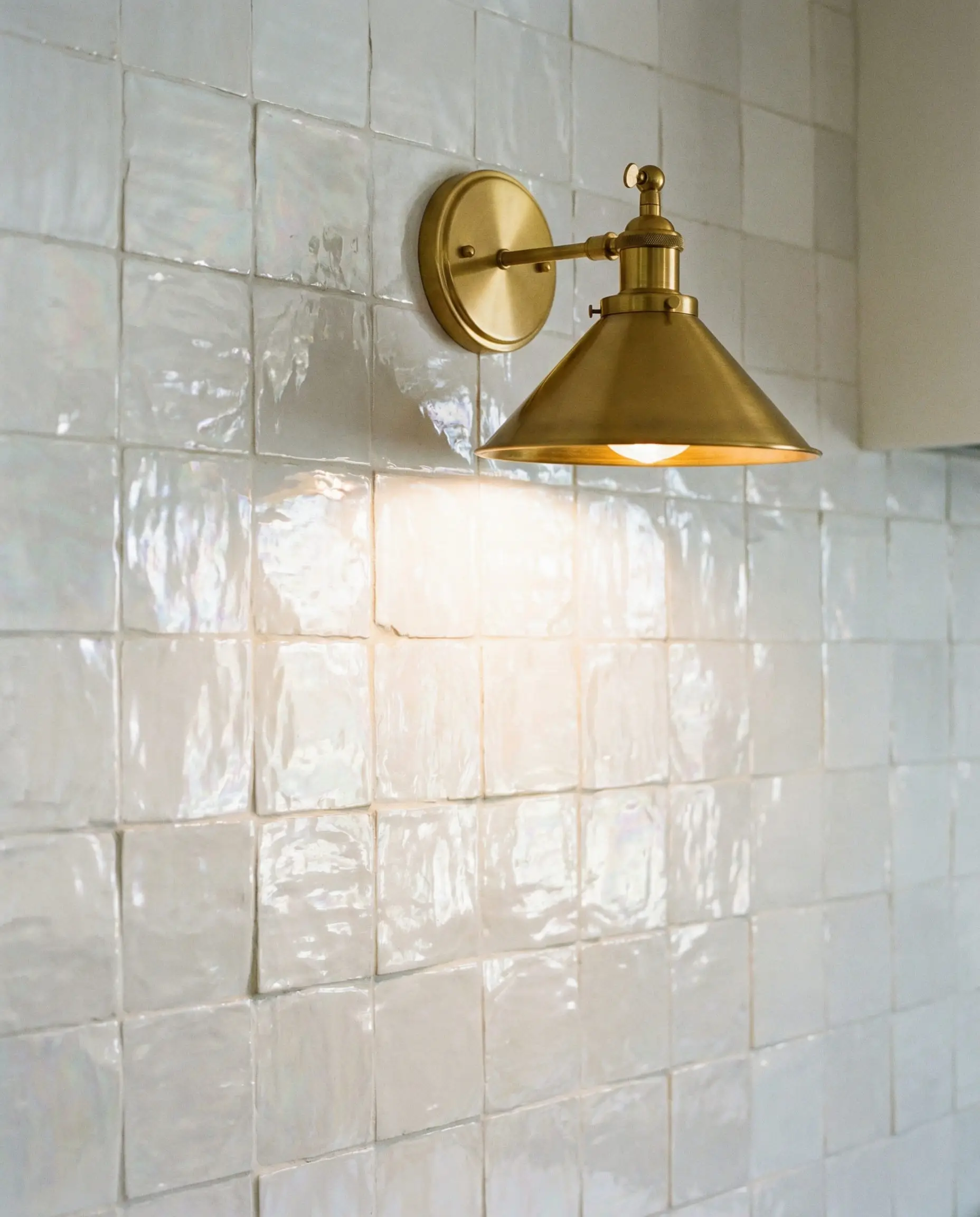 Glossy white Zellige tile backsplash illuminated by a warm gold wall sconce.