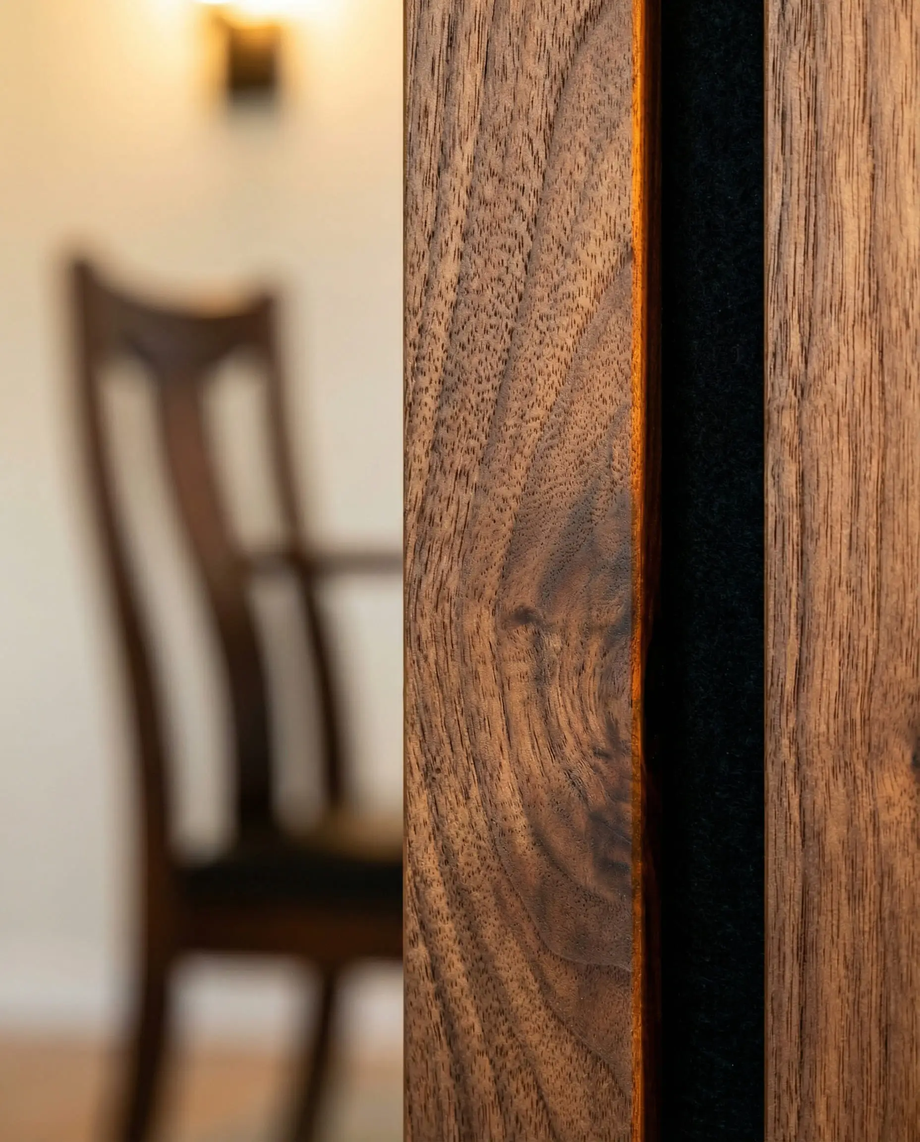 Macro close-up of walnut wood wall slats showing natural grain and black acoustic felt backing with warm lighting highlights.