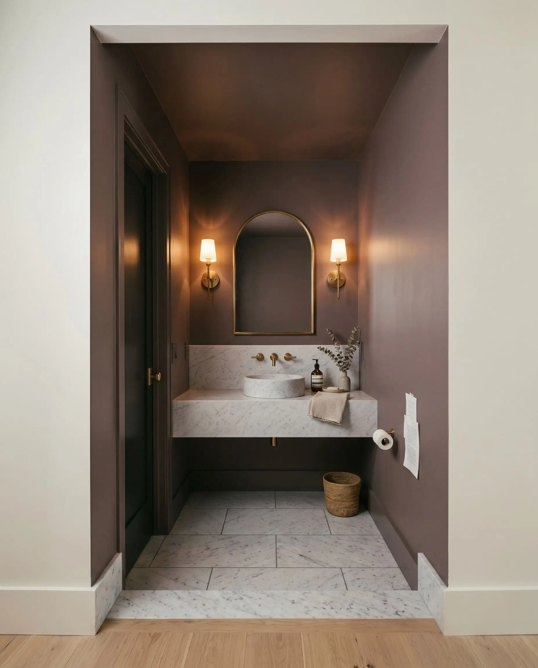 Brass wall sconces frame a honed Carrara marble vanity in a windowless powder room featuring color-drenched subdued rose-violet walls and ceiling.