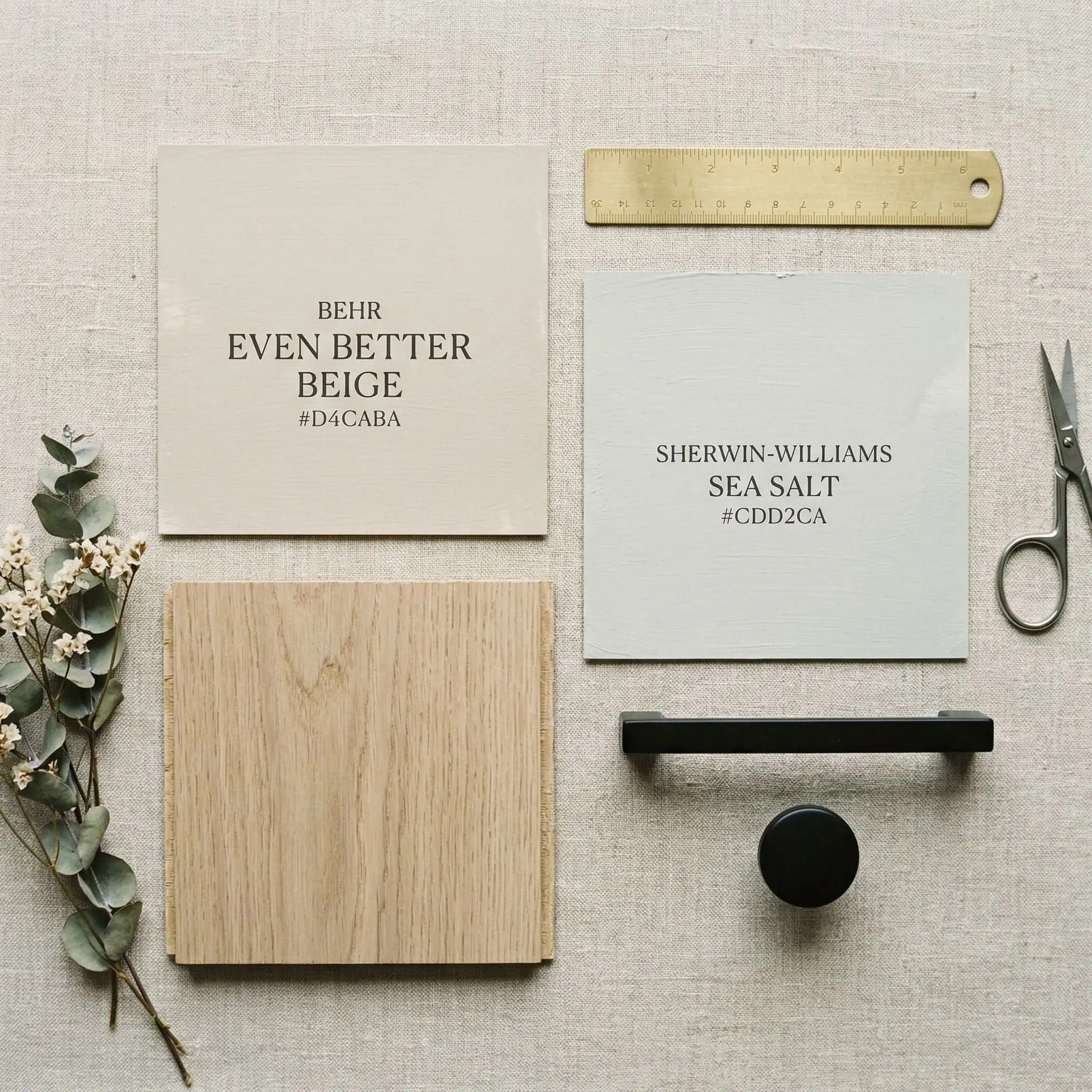 A curated architectural flat-lay features a painted color card of Behr Even Better Beige (Hex #D4CABA) alongside a Sherwin-Williams Sea Salt swatch, white oak flooring, and matte black hardware.