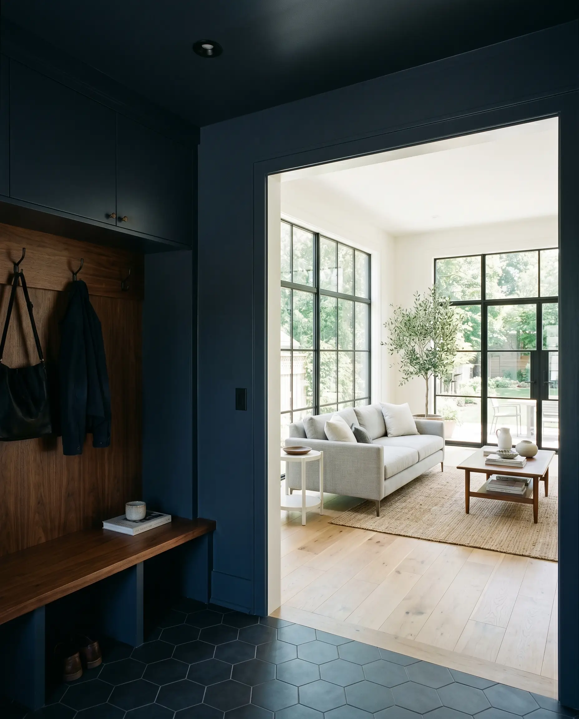 A dramatic mudroom vestibule drenched in Sherwin-Williams Sea Mariner (Hex #434A54) features a warm walnut bench and opens into a bright, light-filled living space.