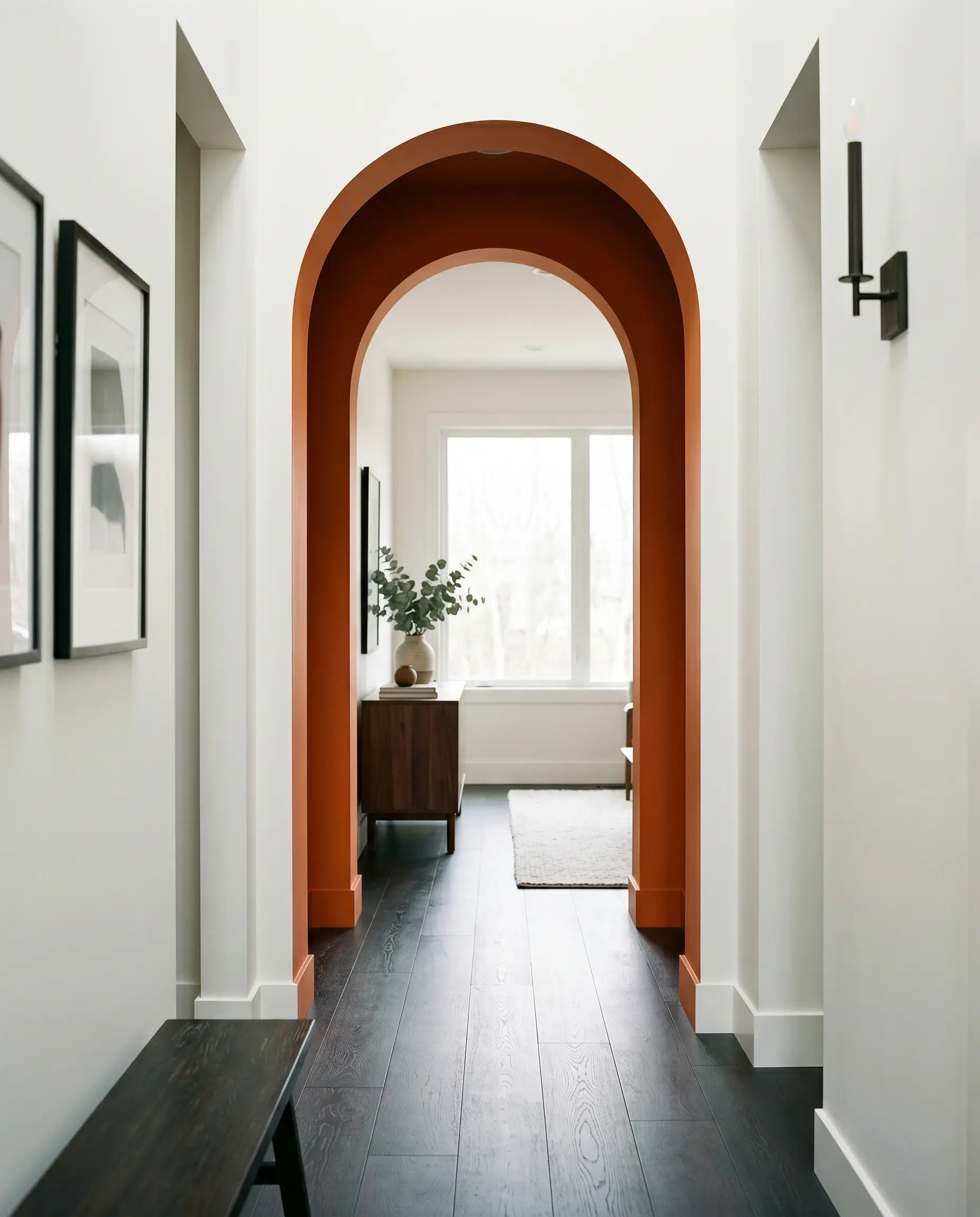 A deeply saturated warm orange paints the interior casing of a narrow transitional archway, framed by soft white living space walls and dark matte flooring.