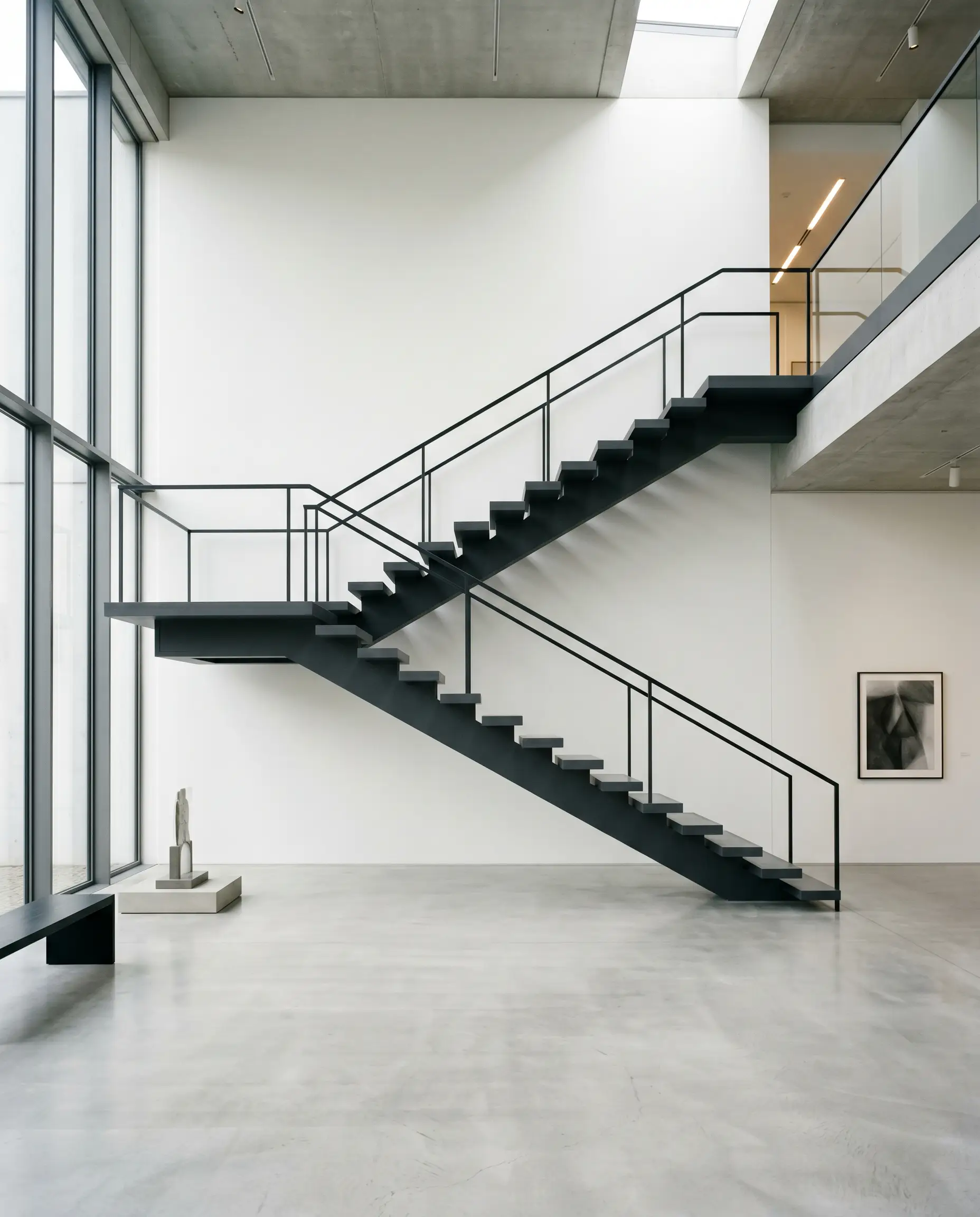 A monolithic floating staircase features structural stringers and open-riser treads finished in a deep chromatic black set against a stark white gallery wall.