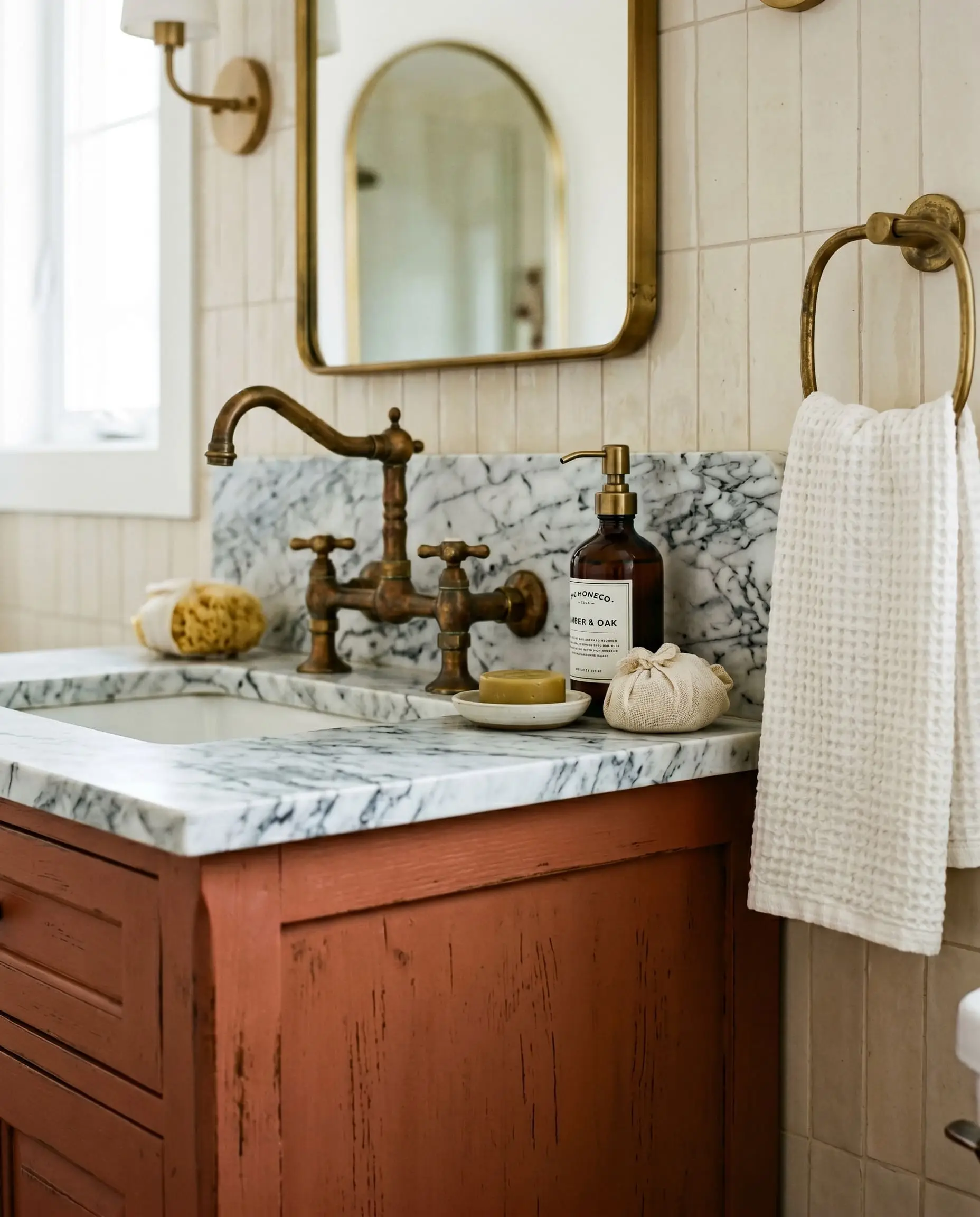 A patinaed unlacquered brass faucet sits on icy Carrara marble directly above the fiery warmth of an earthy brown painted vanity.
